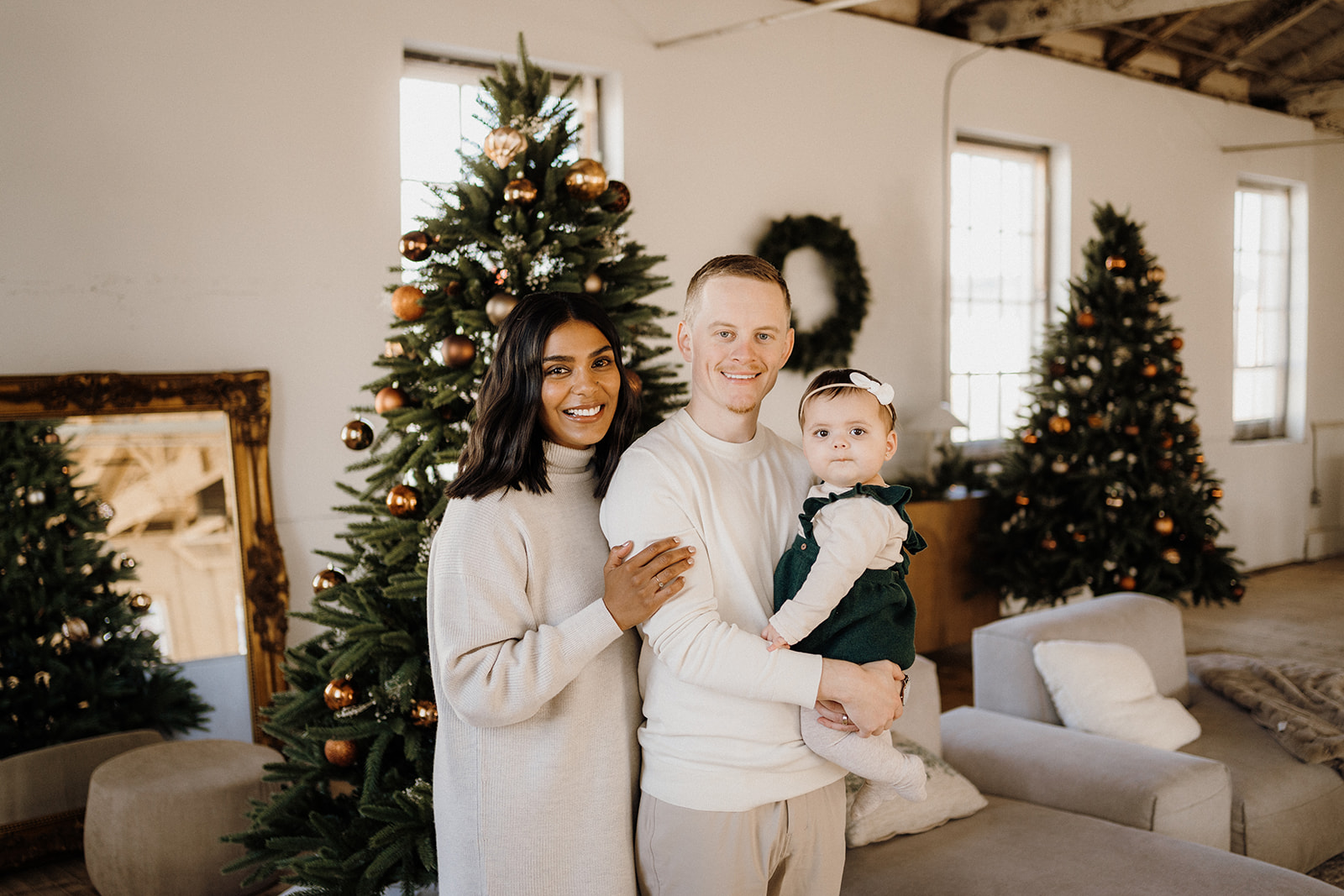 A family of three standing inside in front of a Christmas Tree.