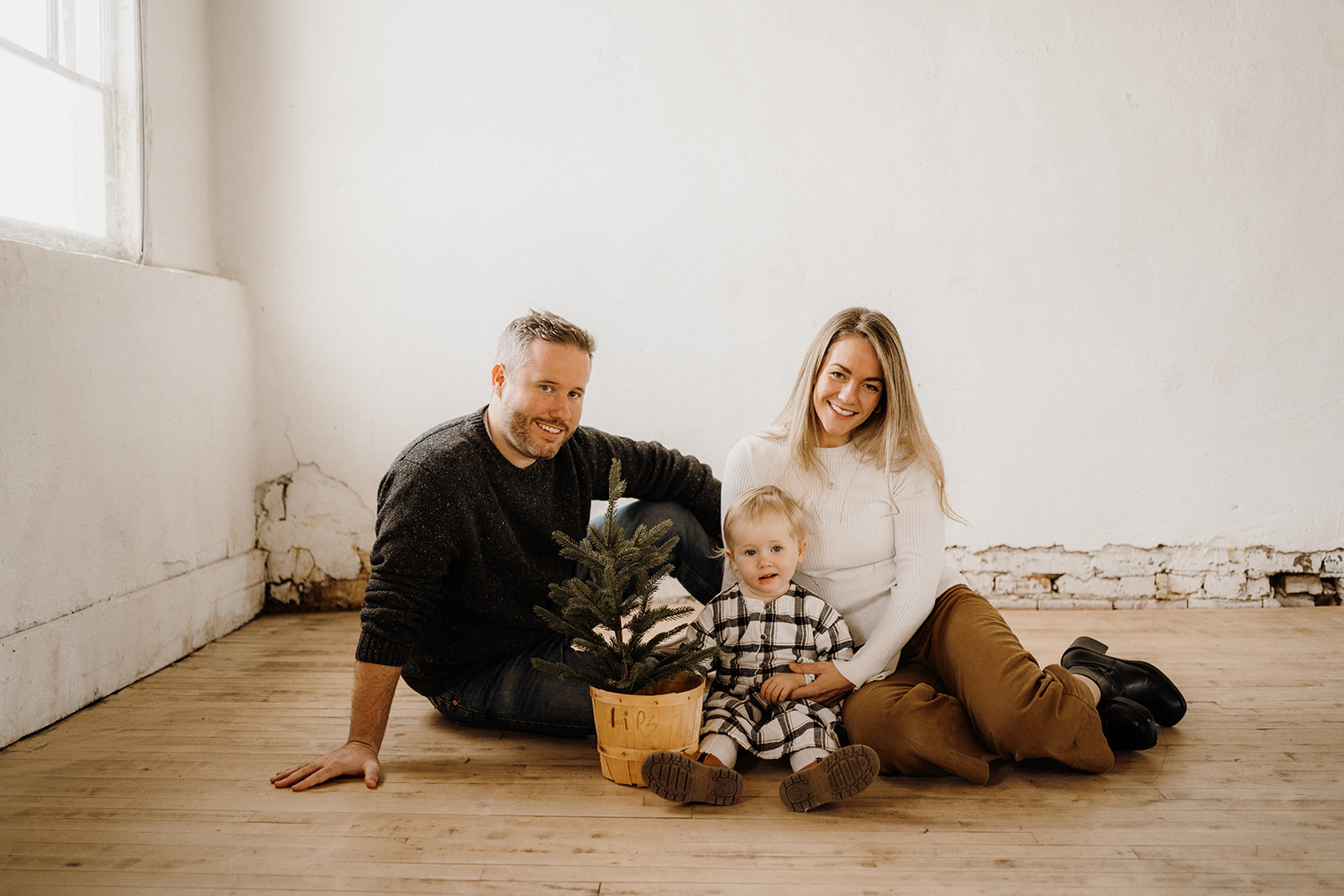 A family of three sitting around a plant inside.