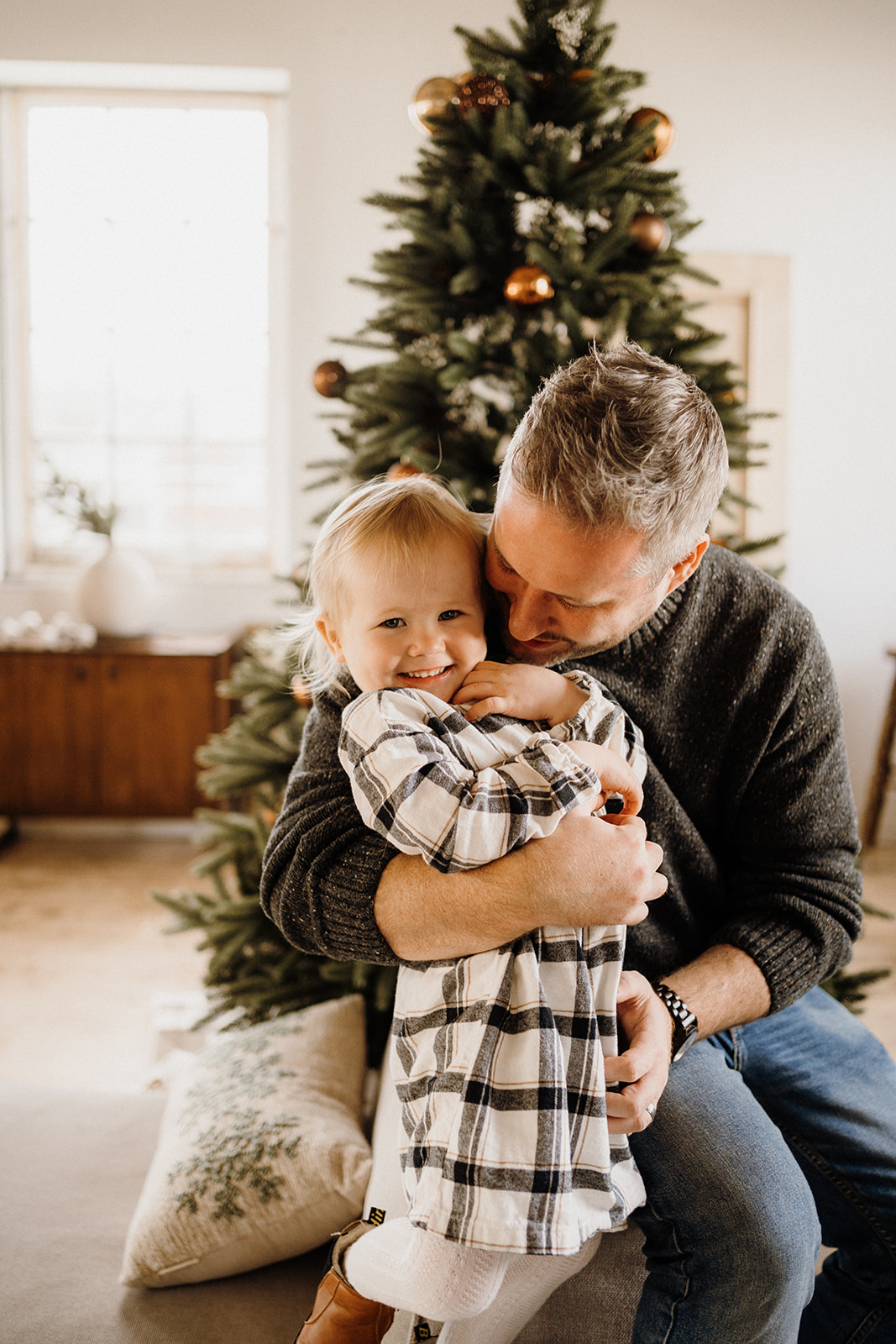 A father hugging their child in front of a Christmas Tree.