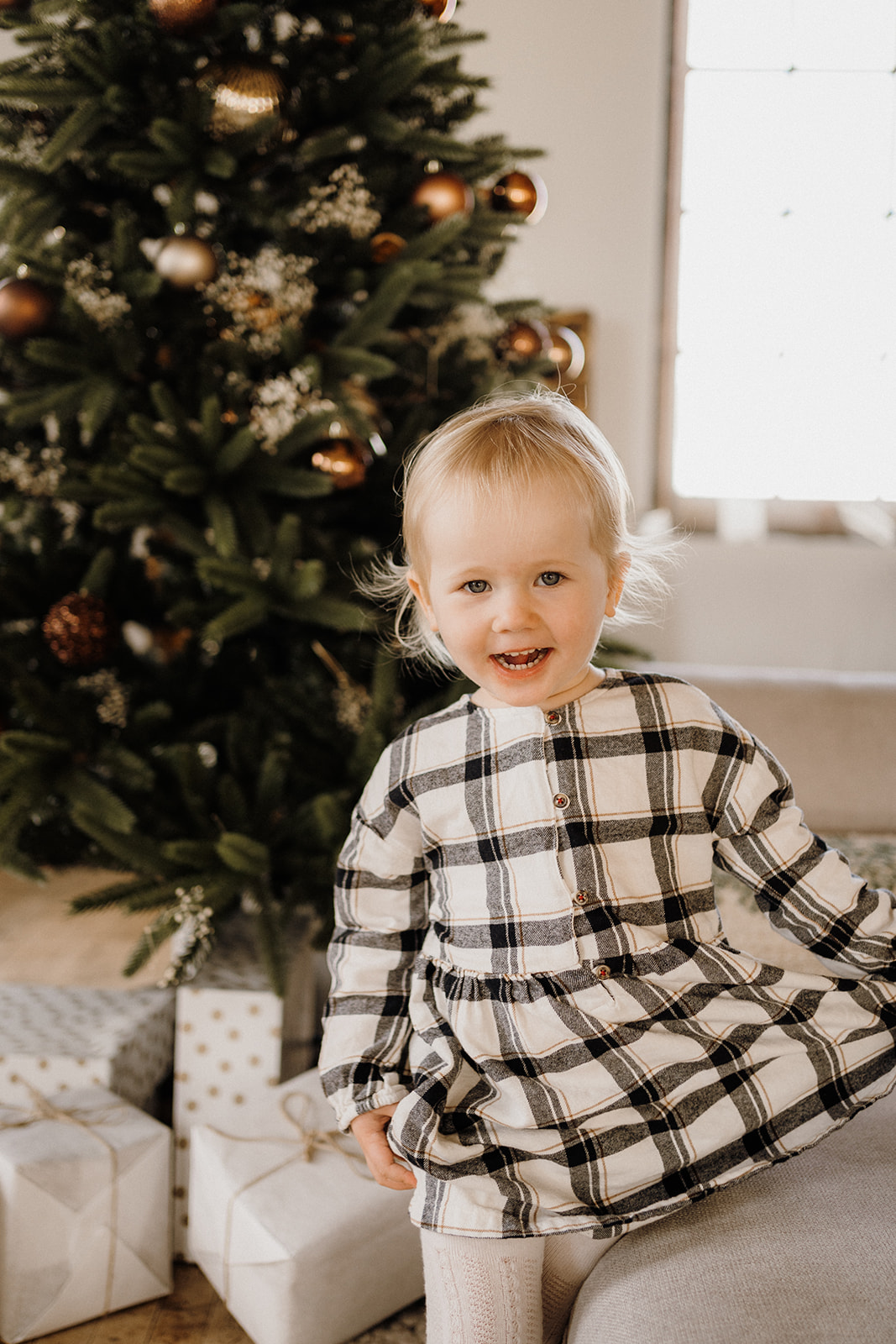 A toddler standing in front of a Christmas Tree.