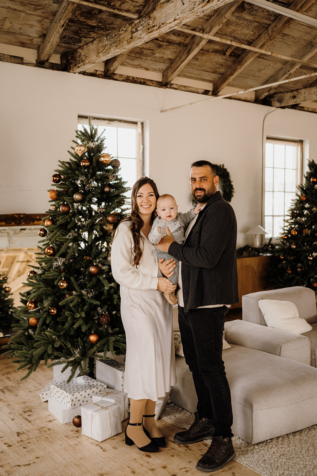 A family of three inside beside a Christmas Tree.
