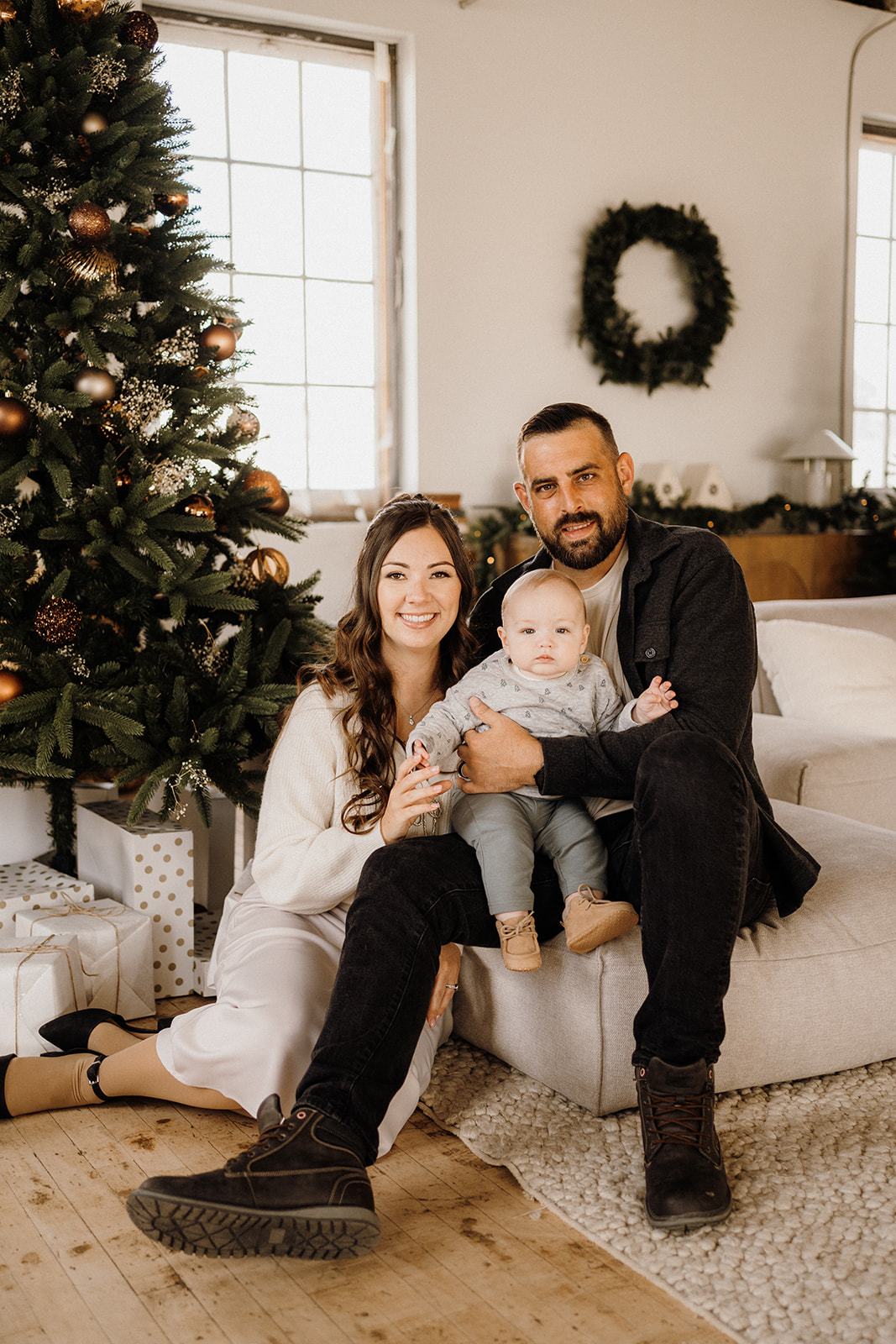A family of three inside beside a Christmas Tree.