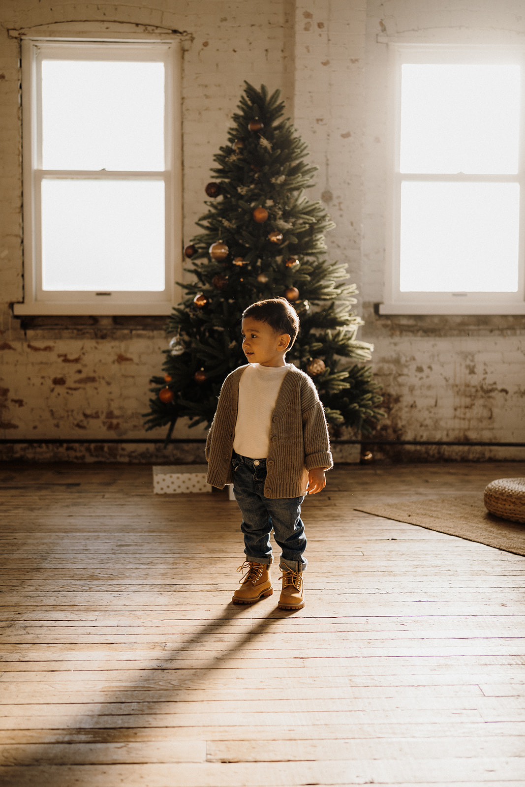 A child standing in front of a Christmas Tree inside.