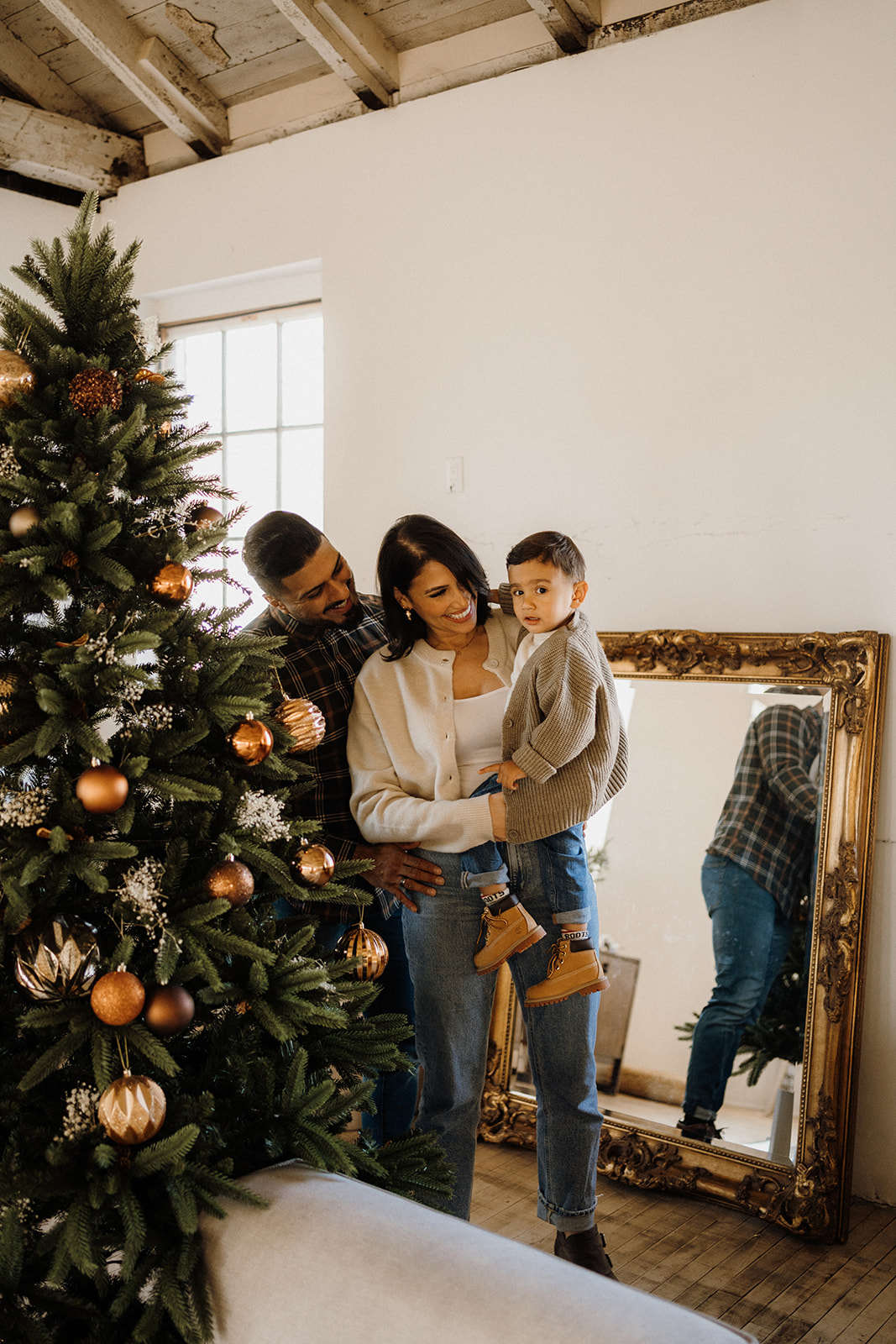 A family of three standing behind a Christmas Tree.