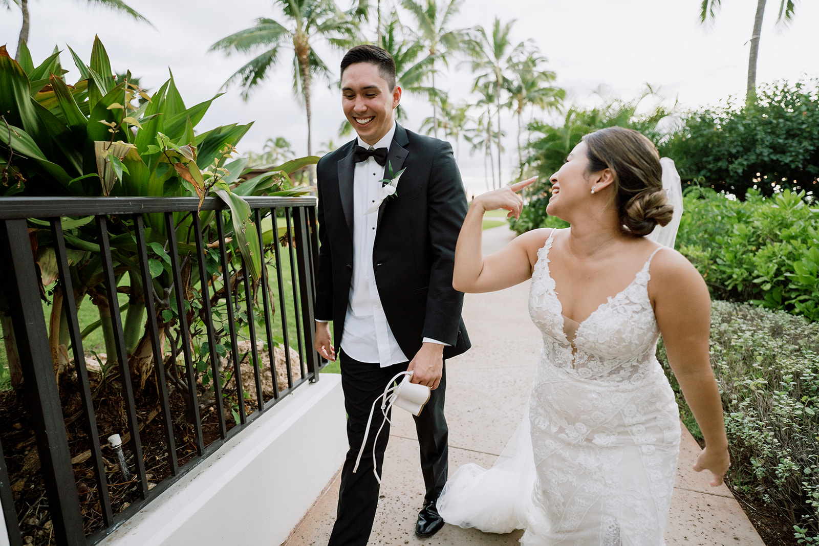 A bride and groom walking down a walkway with palm trees in the background at the Four Seasons Oahu