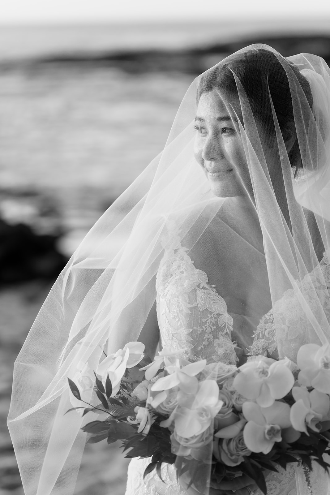 A monochrome photo of the bride wearing a wedding veil on the beach.