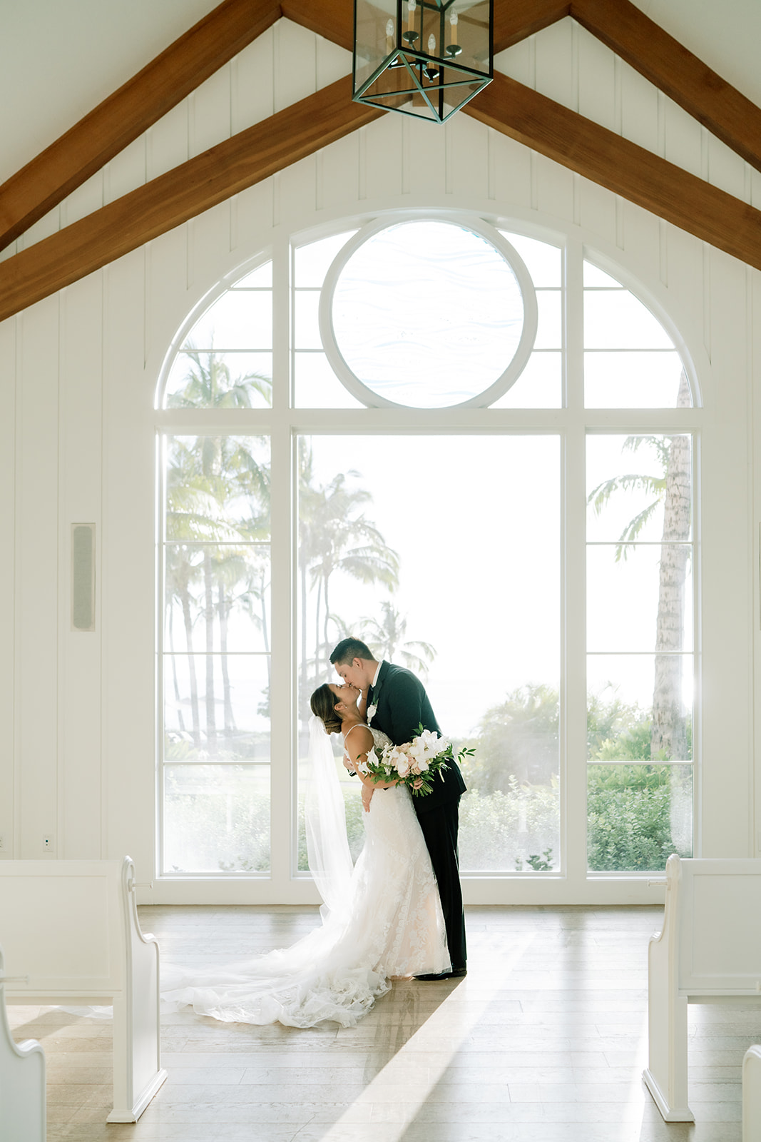 A bride and groom kissing by the big church window of The Four Seasons Oahu Hawaii