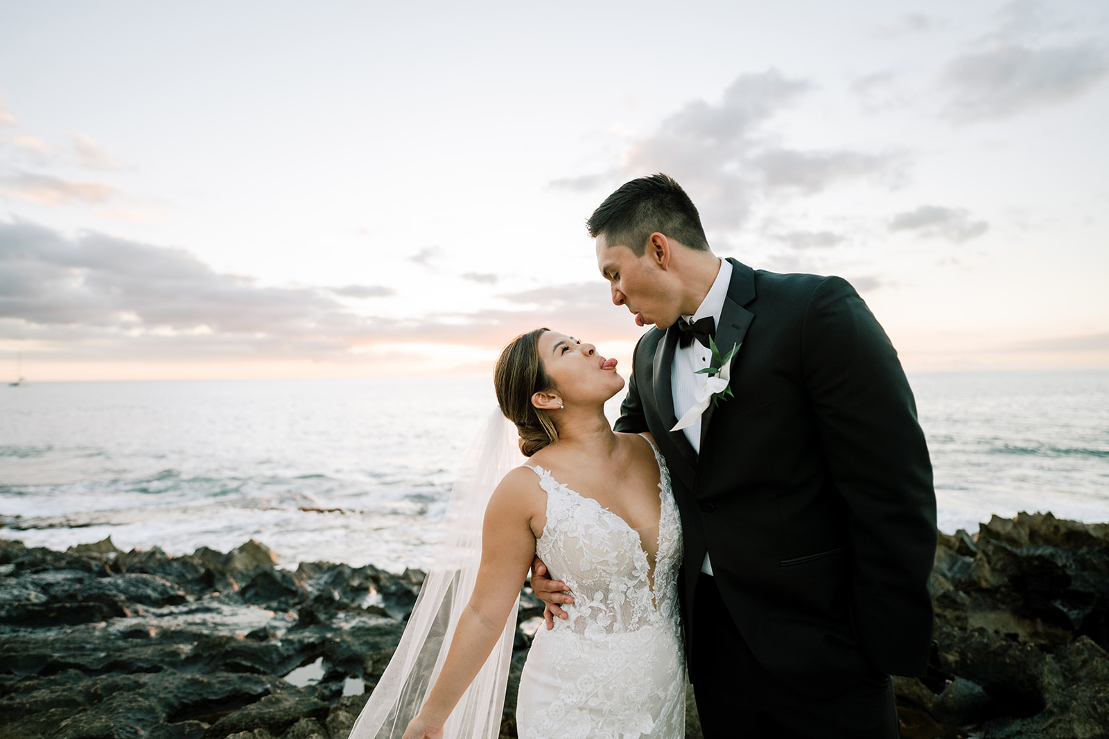A bride and groom standing on the rocks at sunset on Ko'olina Beach