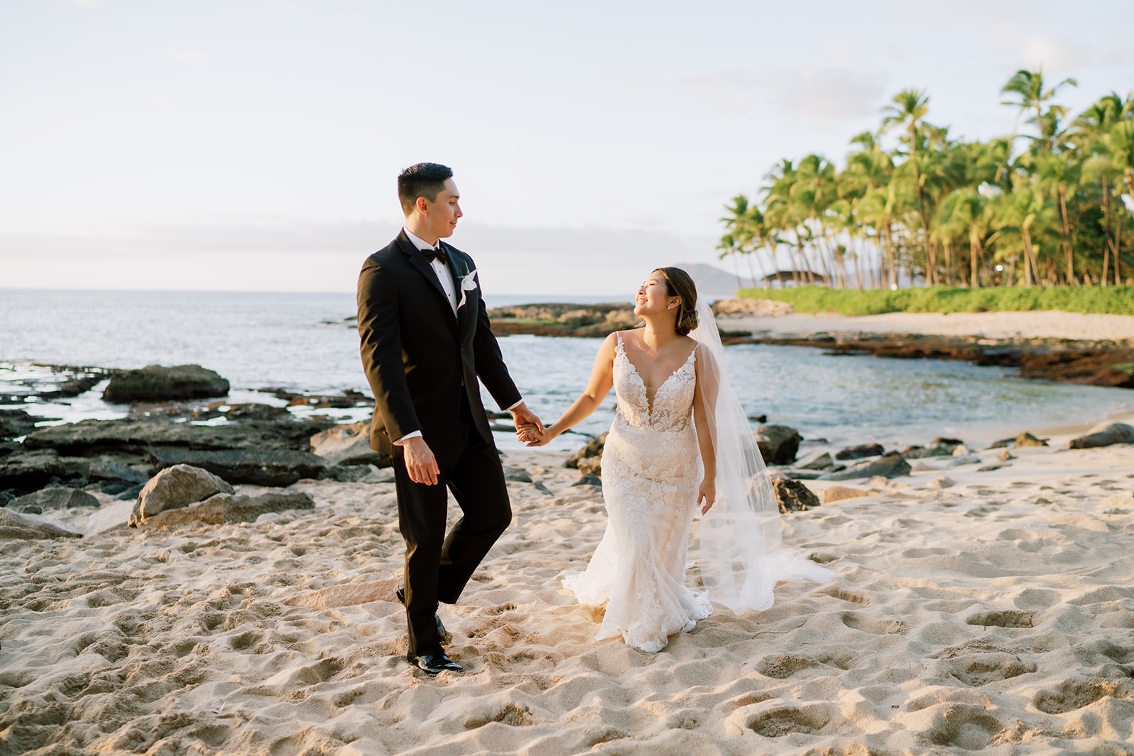 A bride and groom walking on the beach in Oahu