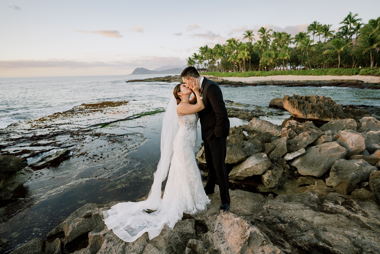 A bride and groom kissing on the rocks during sunset in Oahu Hawaii.
