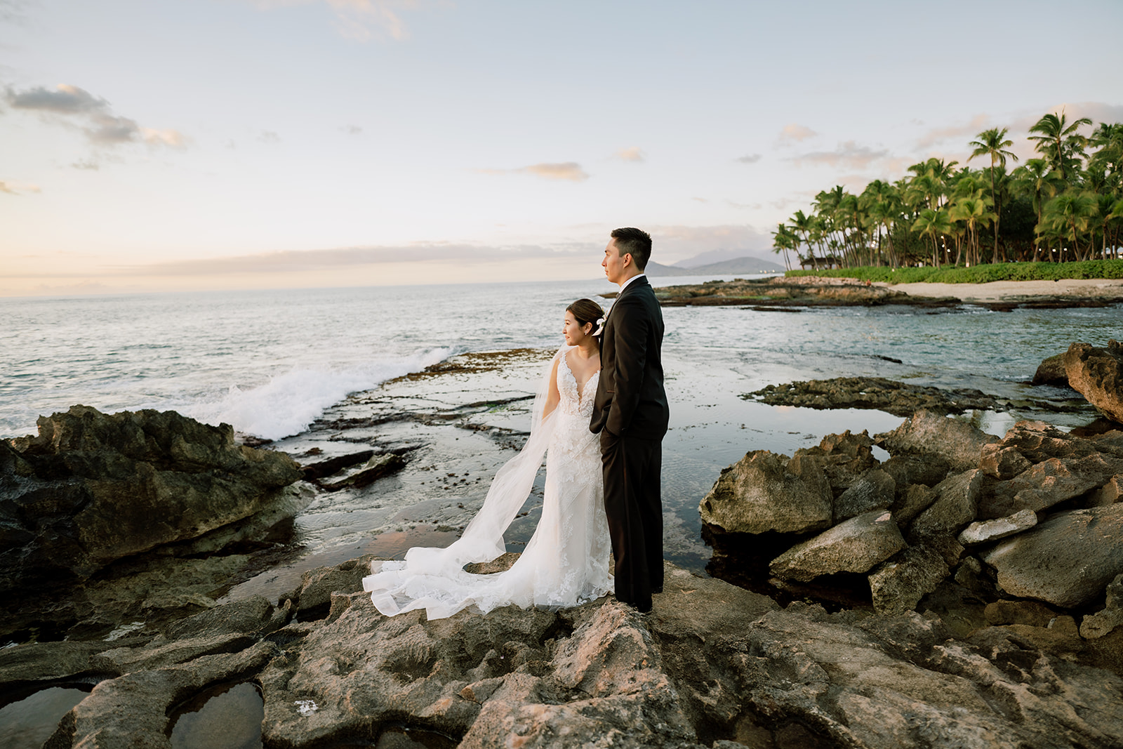 A bride and groom standing on rocks watching the sunset captured by Megan Moura Wedding Photographer