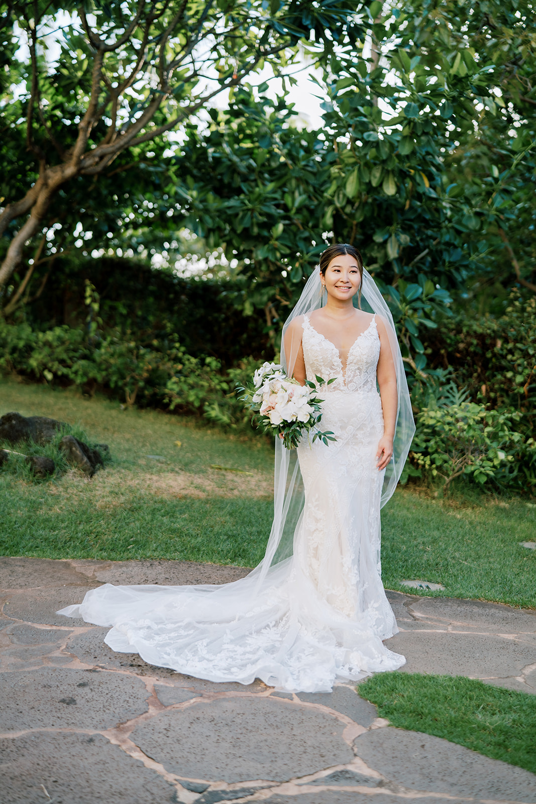 A bride in a white wedding dress standing on a stone path at The Four Seasons Resort Oahu at Ko'olina