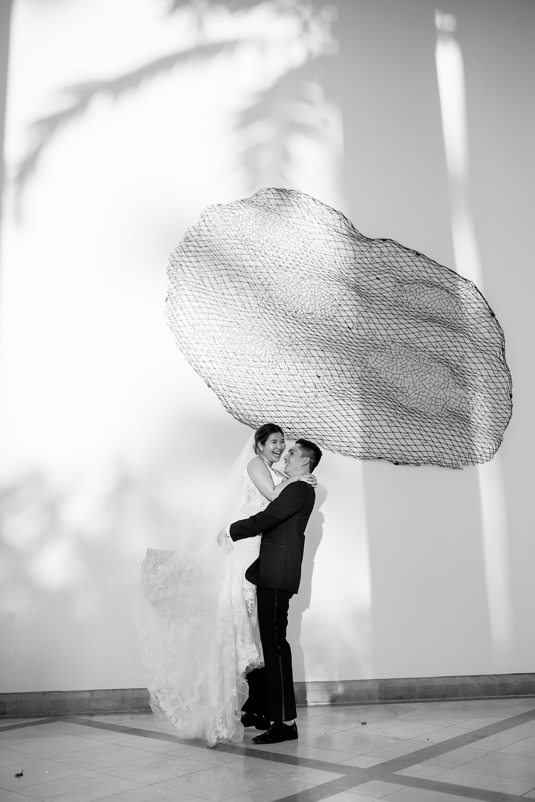 Groom carrying his bride posing in front of a large art at the Four Seasons Resort Oahu