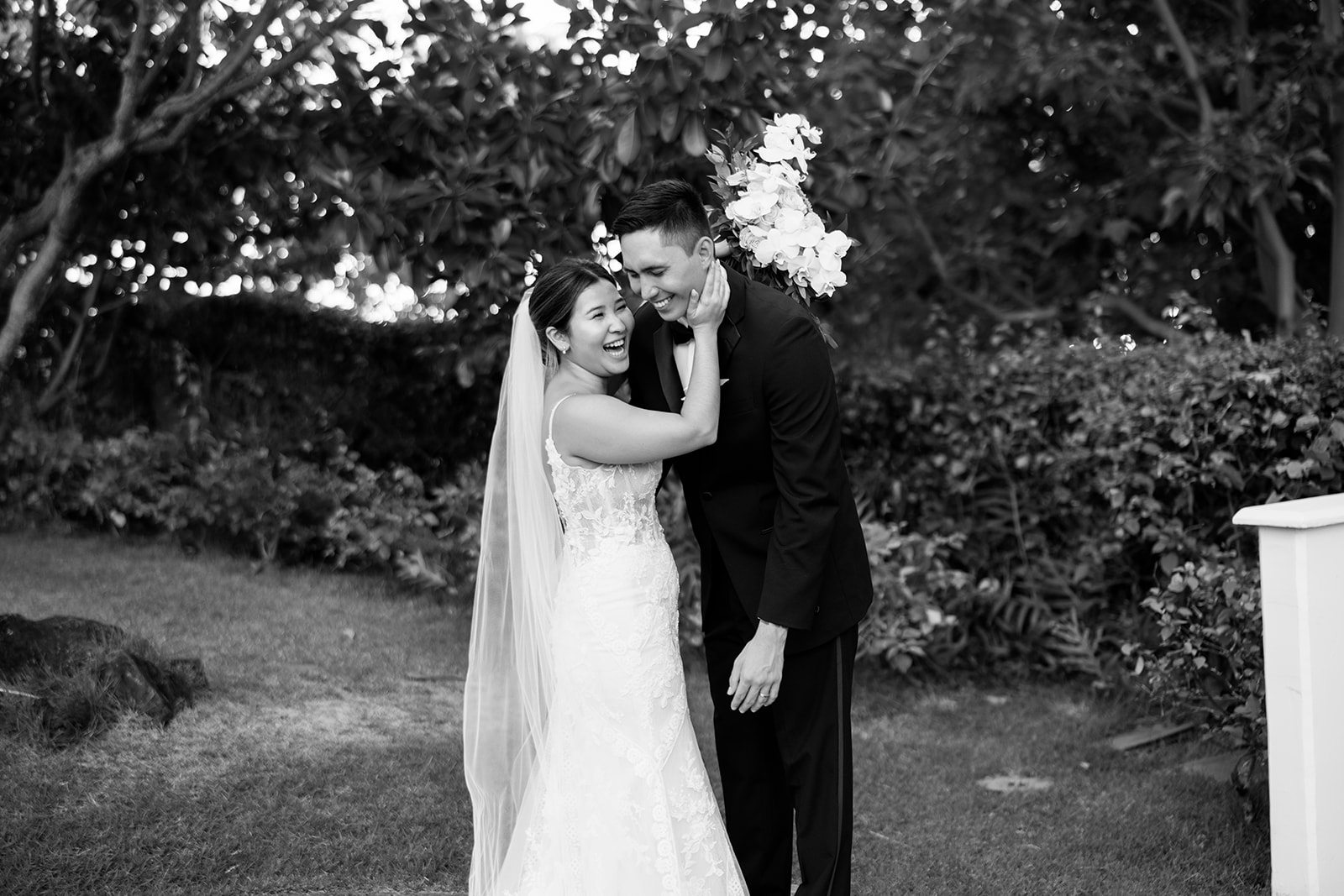 A happy bride and groom hugging in front of bushes.