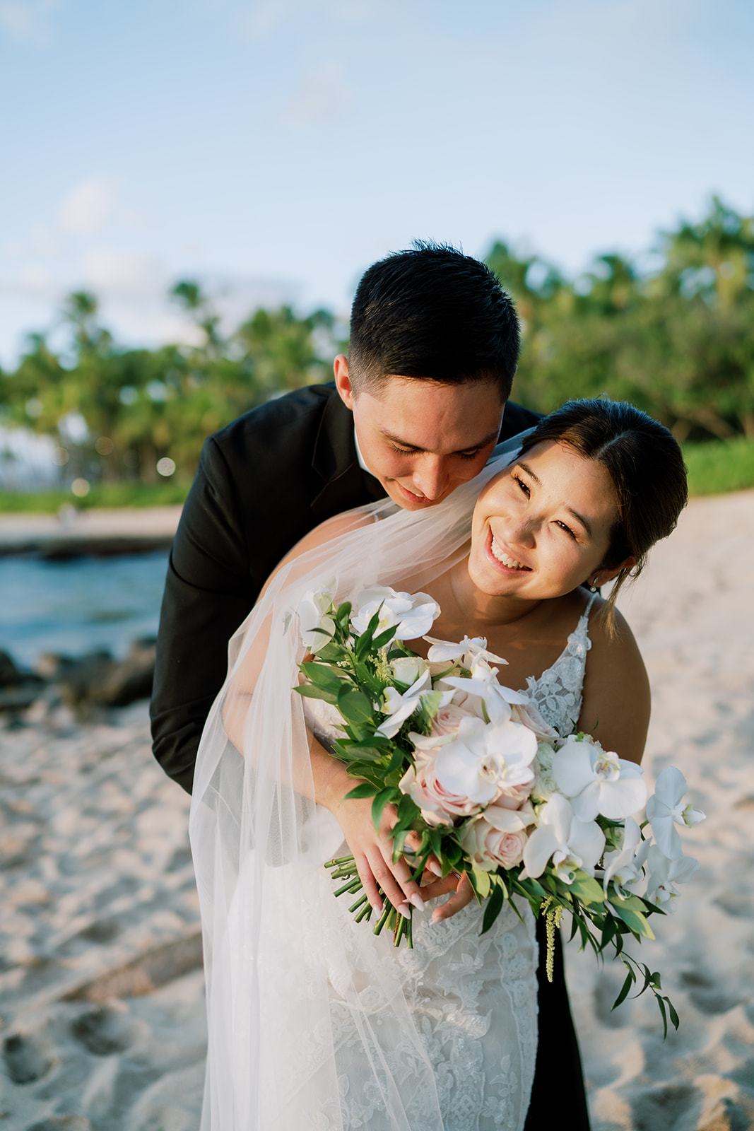 A bride and groom hugging on the Ko'olina beach in Hawaii