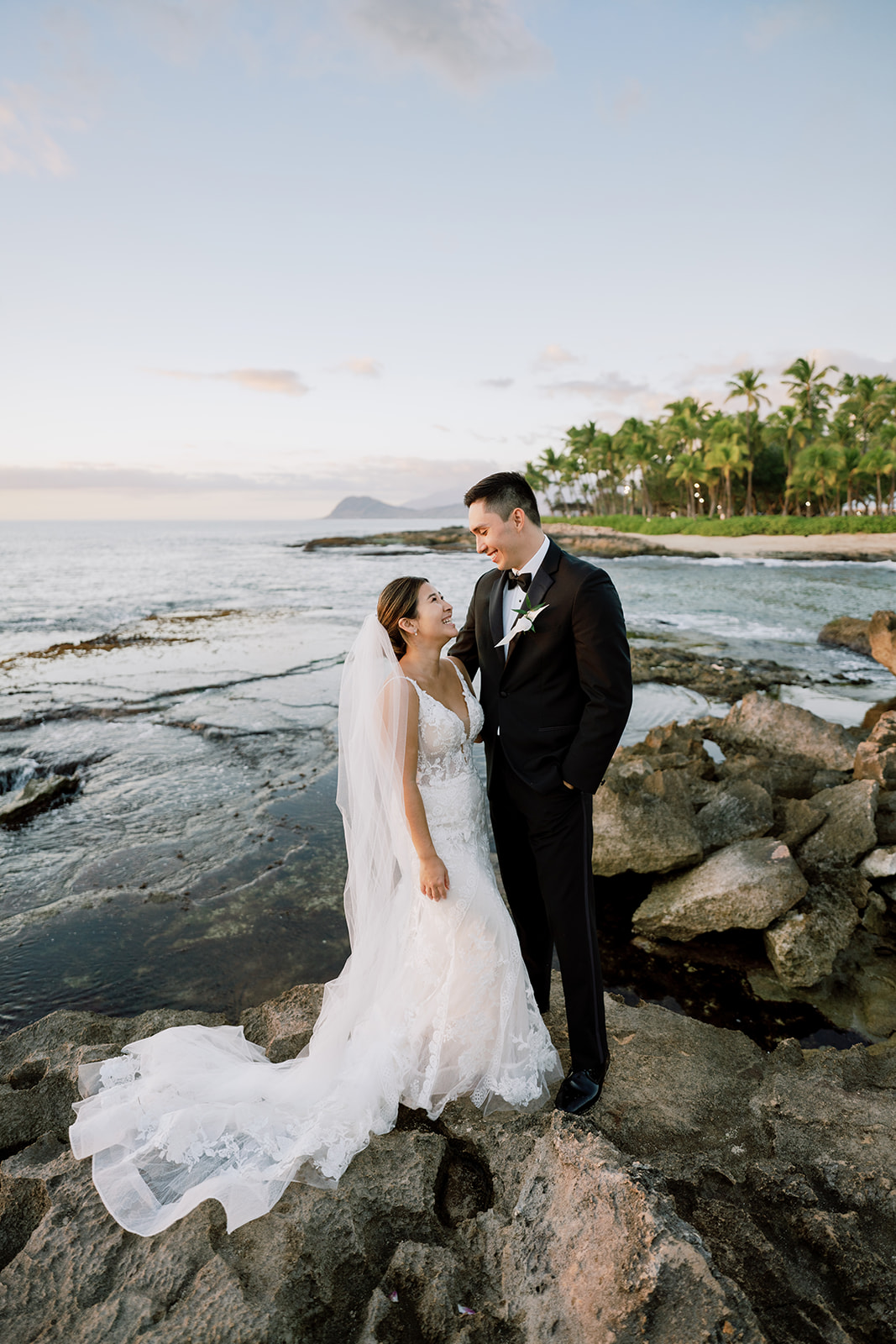 A bride and groom looking at each other near the ocean during sunset at Ko'olina Beach