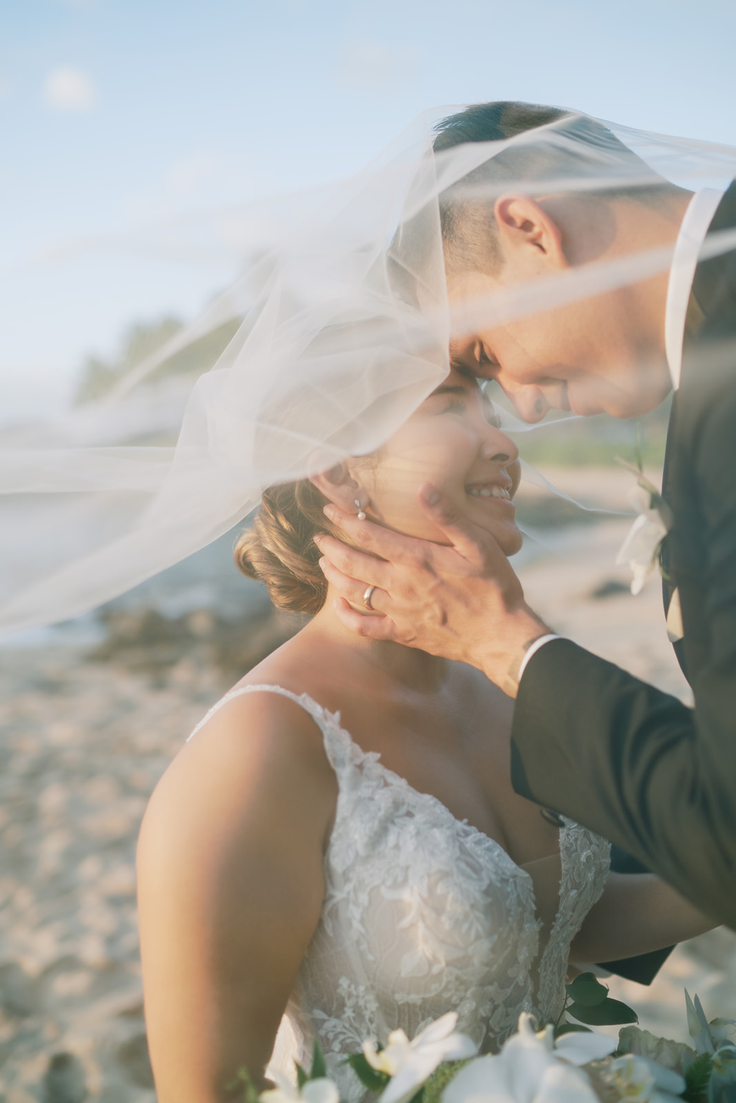 A bride and groom kissing under a veil on the Ko'olina beach taken by Megan Moura Wedding Photographer