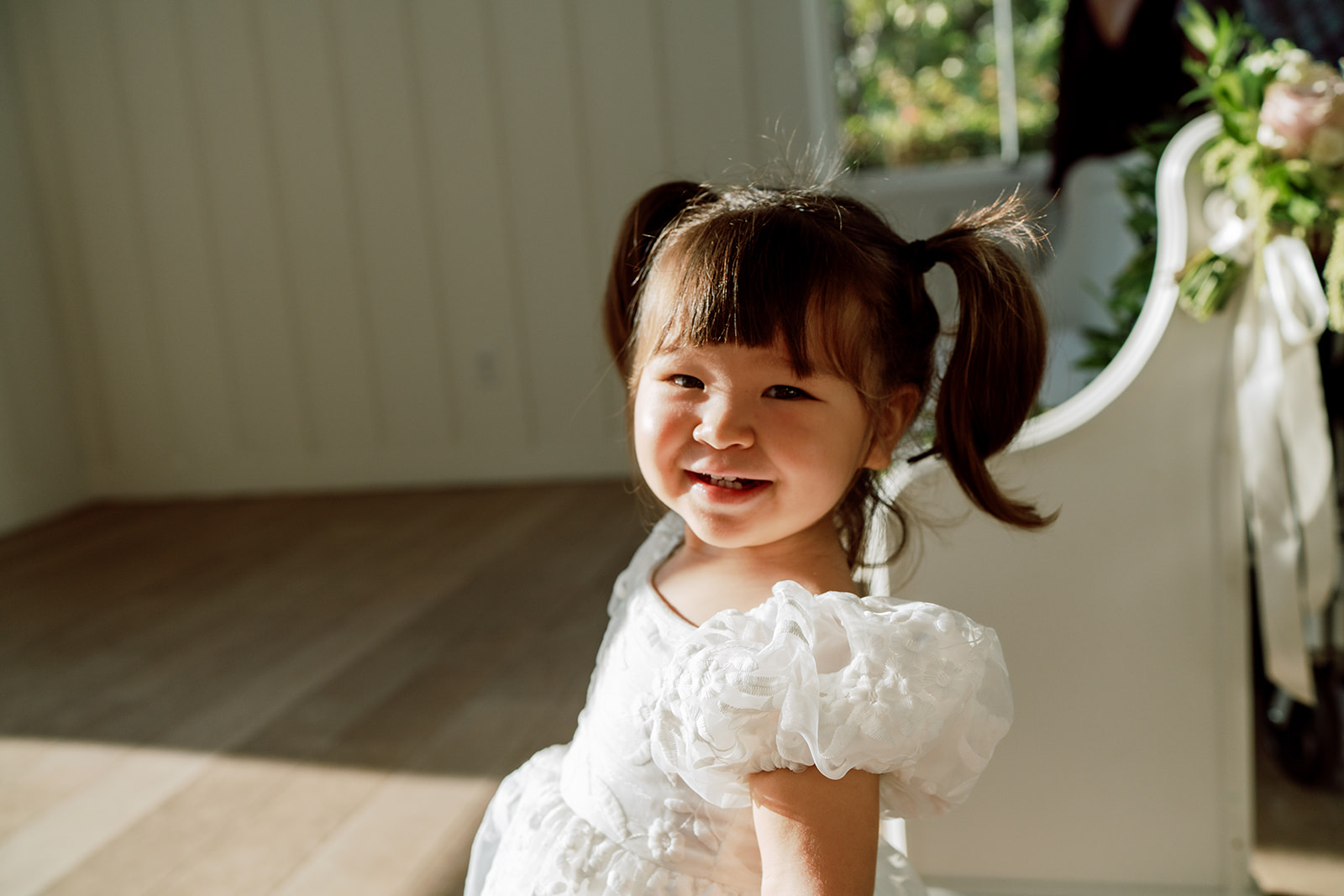 A little girl in a white dress smiles at the camera, wedding in  The Four Seasons by Megan Moura Wedding Photographer