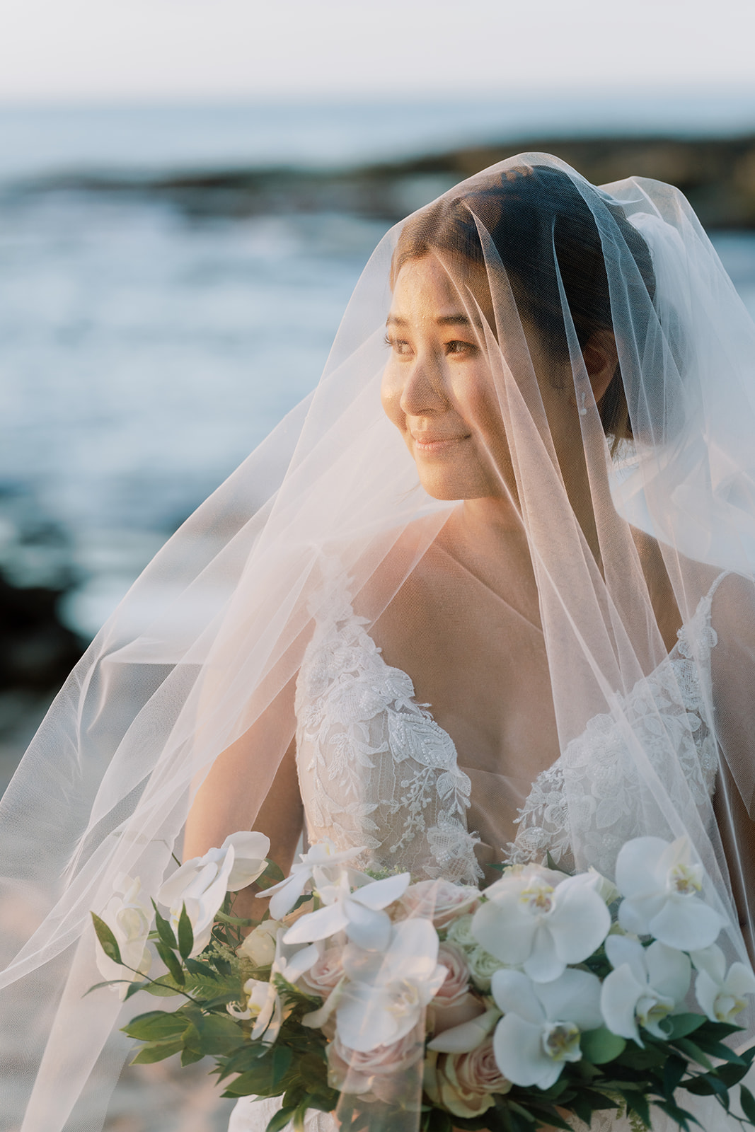 A bride wearing a wedding veil on the beach at the Four Seasons captured by Megan Moura Wedding Photographer