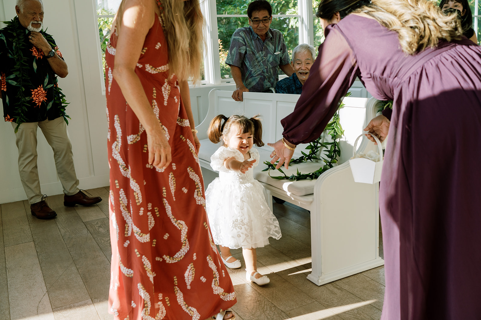 A little girl is being handed a flower by a woman in a purple dress during a wedding in The Four Seasons Oahu
