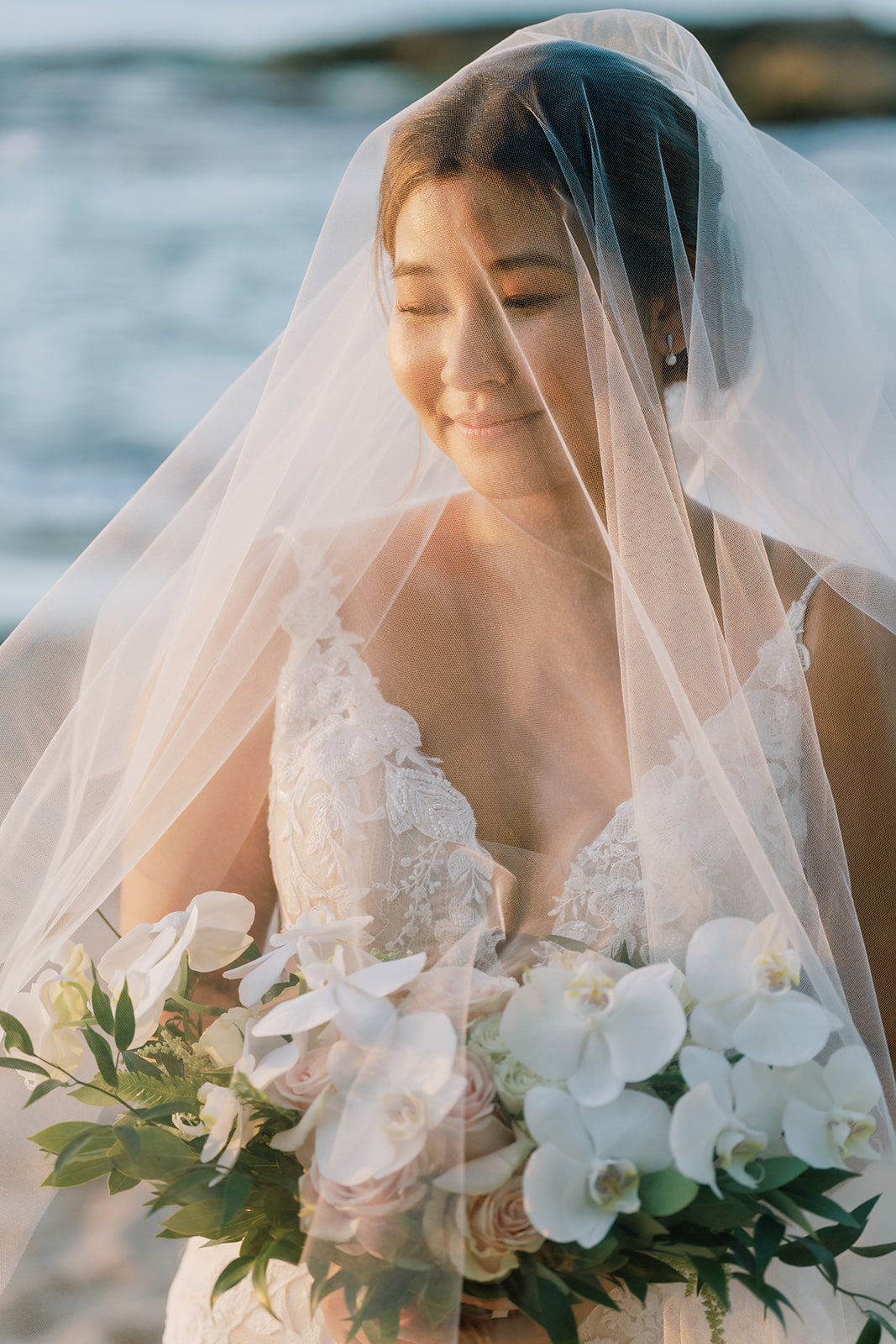 A bride wearing a wedding veil on the beach taken by Megan Moura Wedding Photographer.