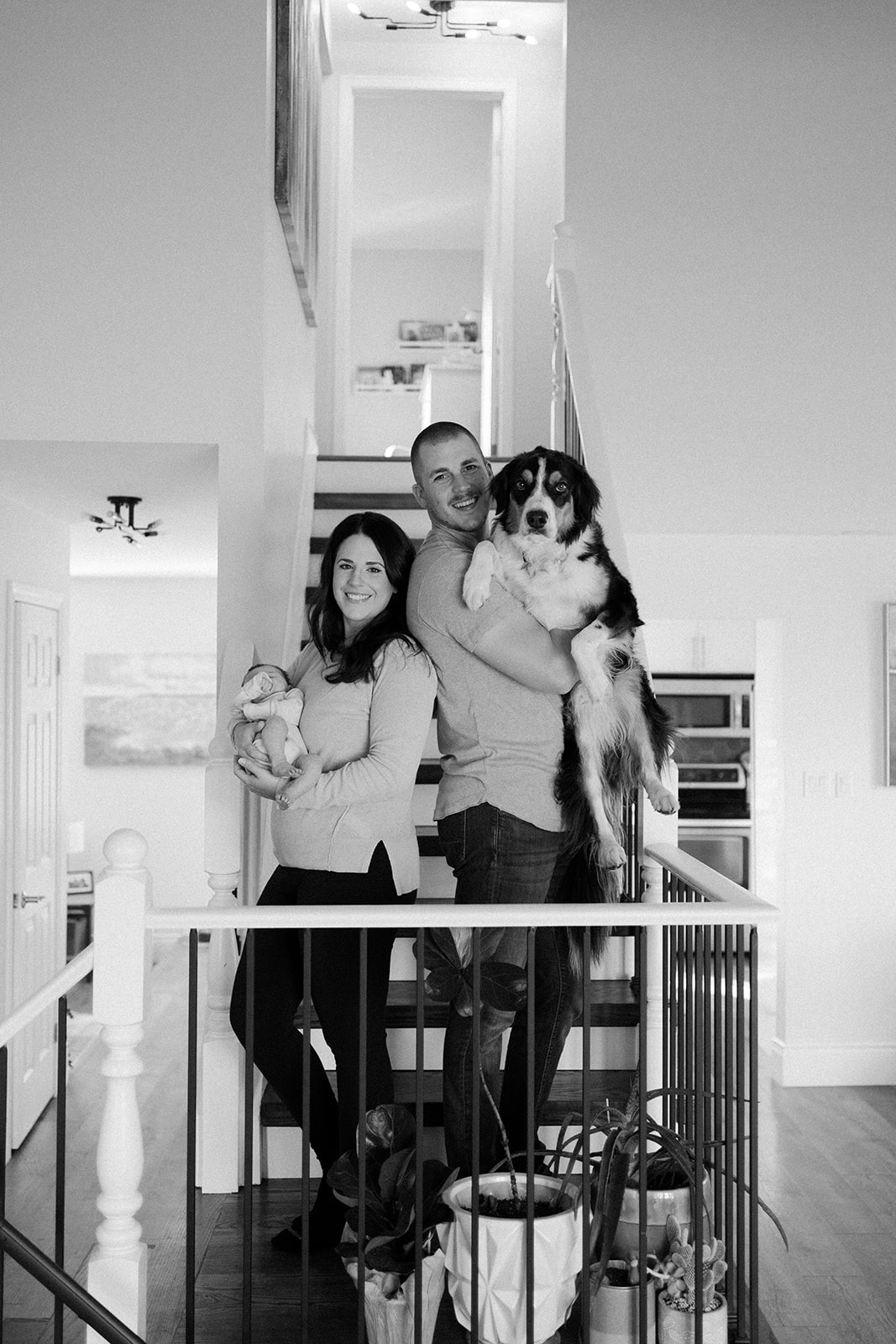 Family standing on the stairs with newborn in moms arms and puppy in dads arms.