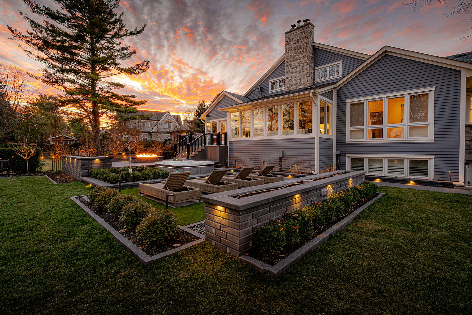 A backyard with lights on in the house and a sunset in the background.