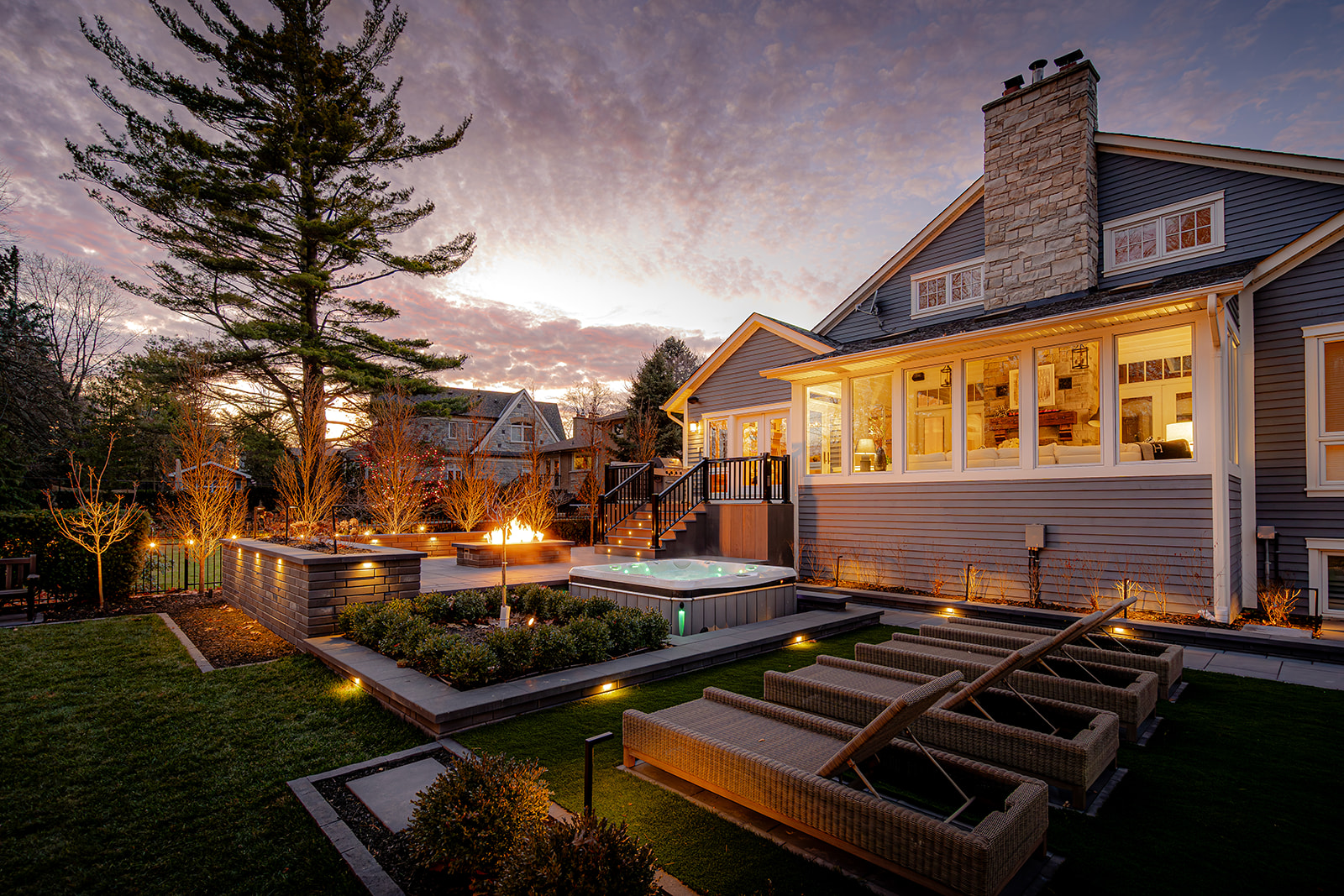 A backyard with lights on in the house and a sunset in the background.