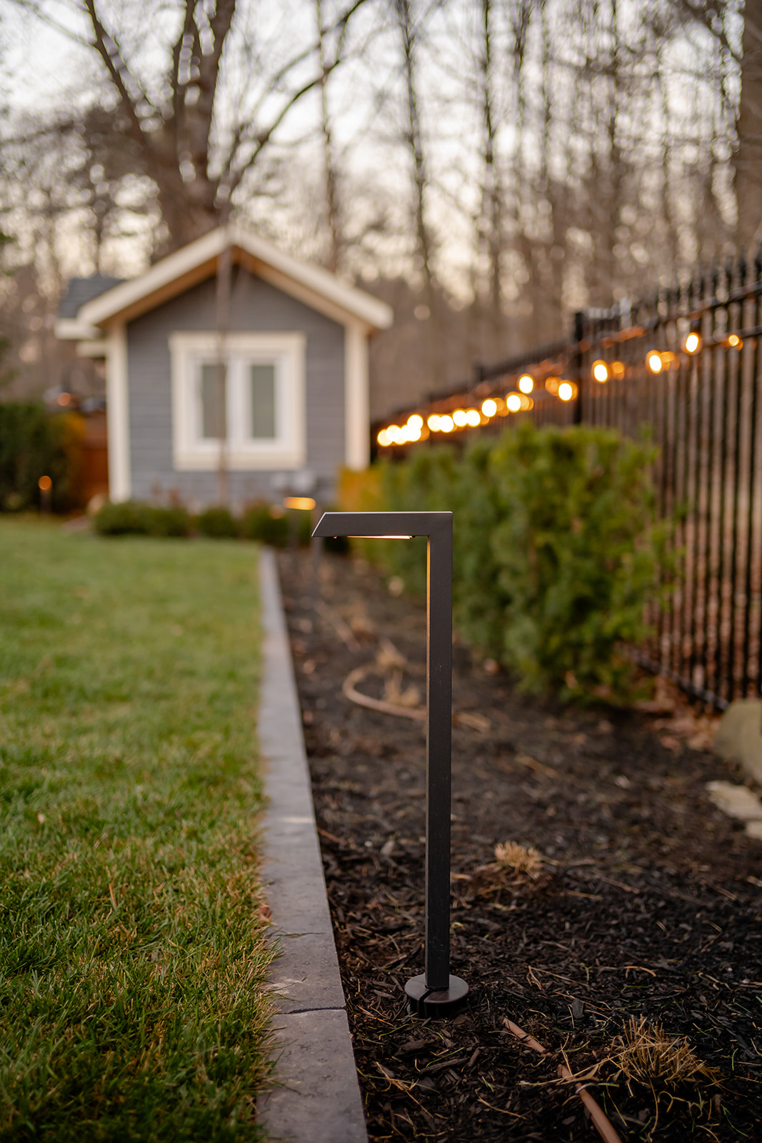 A small lamp planted in the garden with the pool house in the backyard.