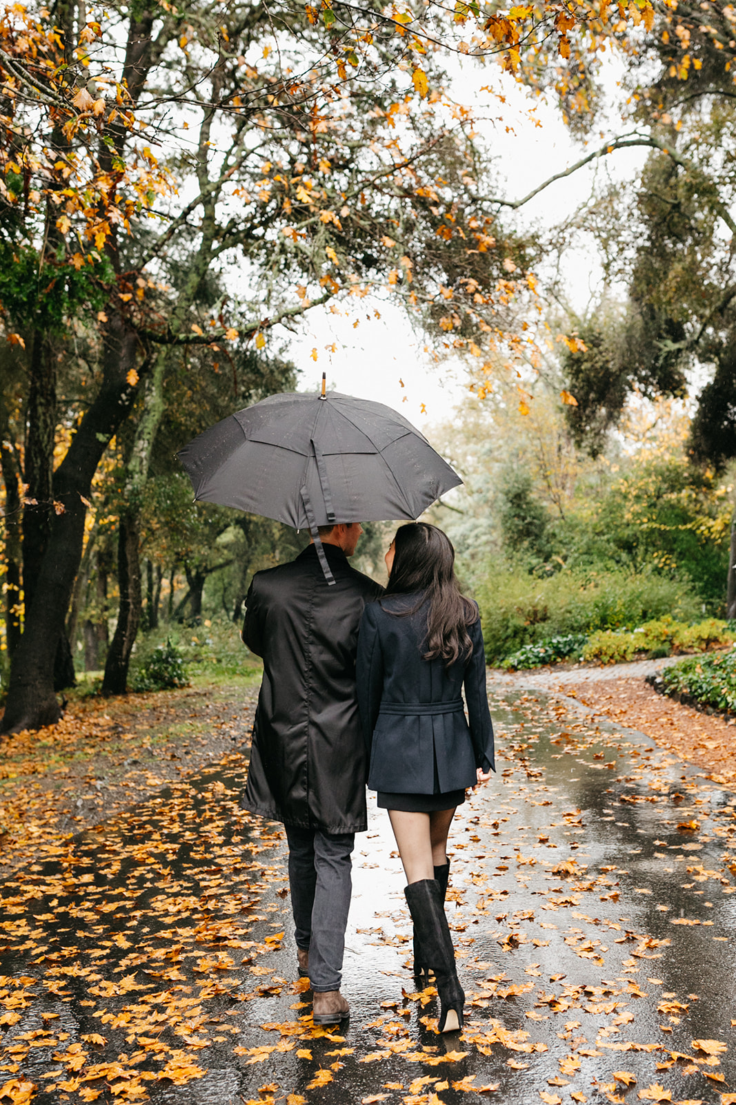 walking together under an umbrella for engagement session photos at the madrona