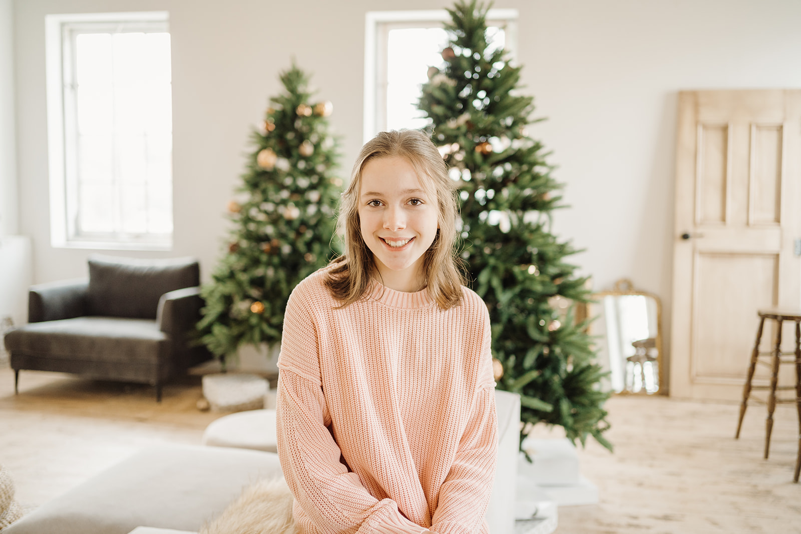 A girl sitting on the edge of a couch in front of a Christmas Tree.