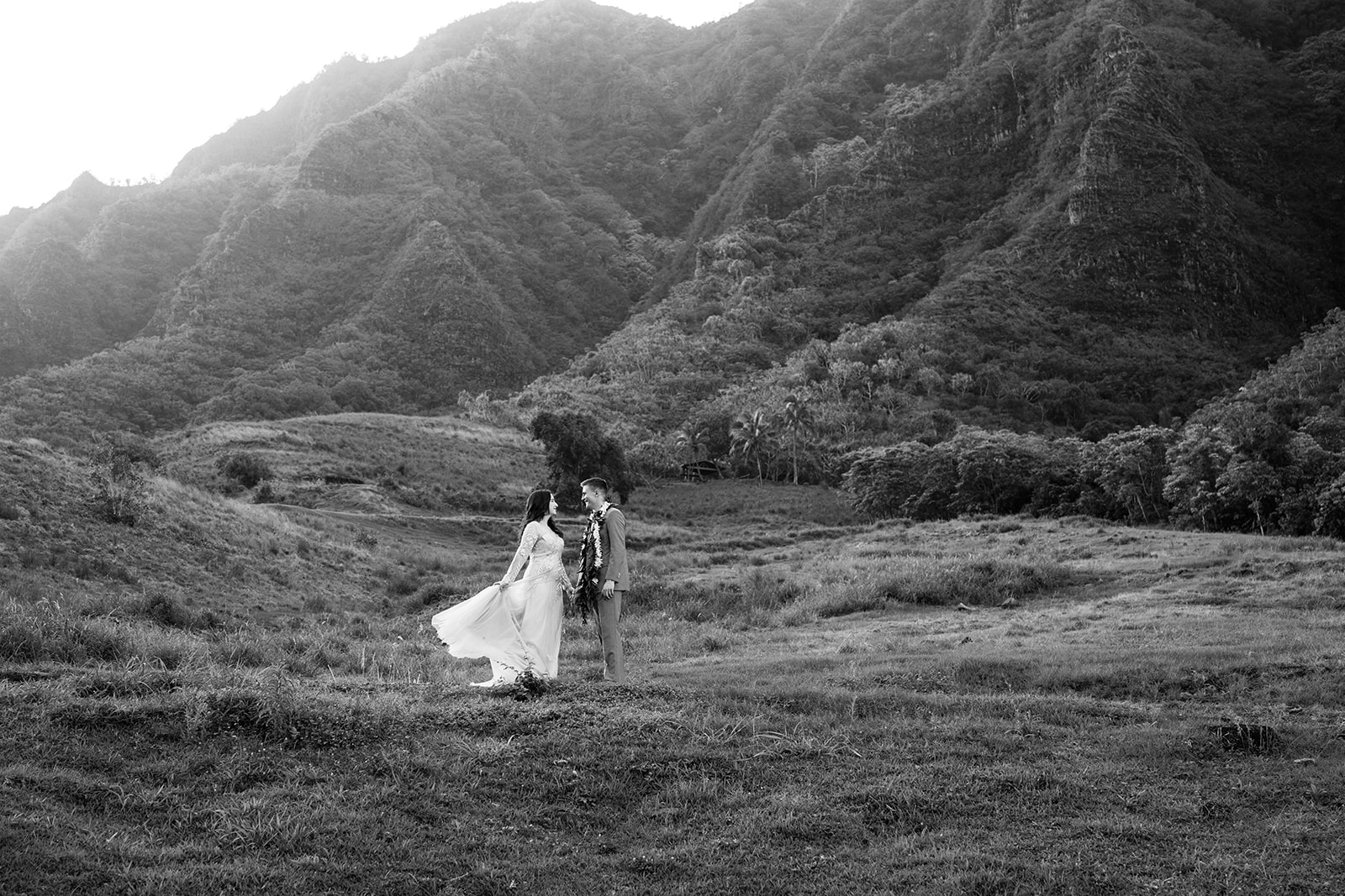 A black and white photo of a bride and groom standing in a field at their Kualoa Ranch wedding.