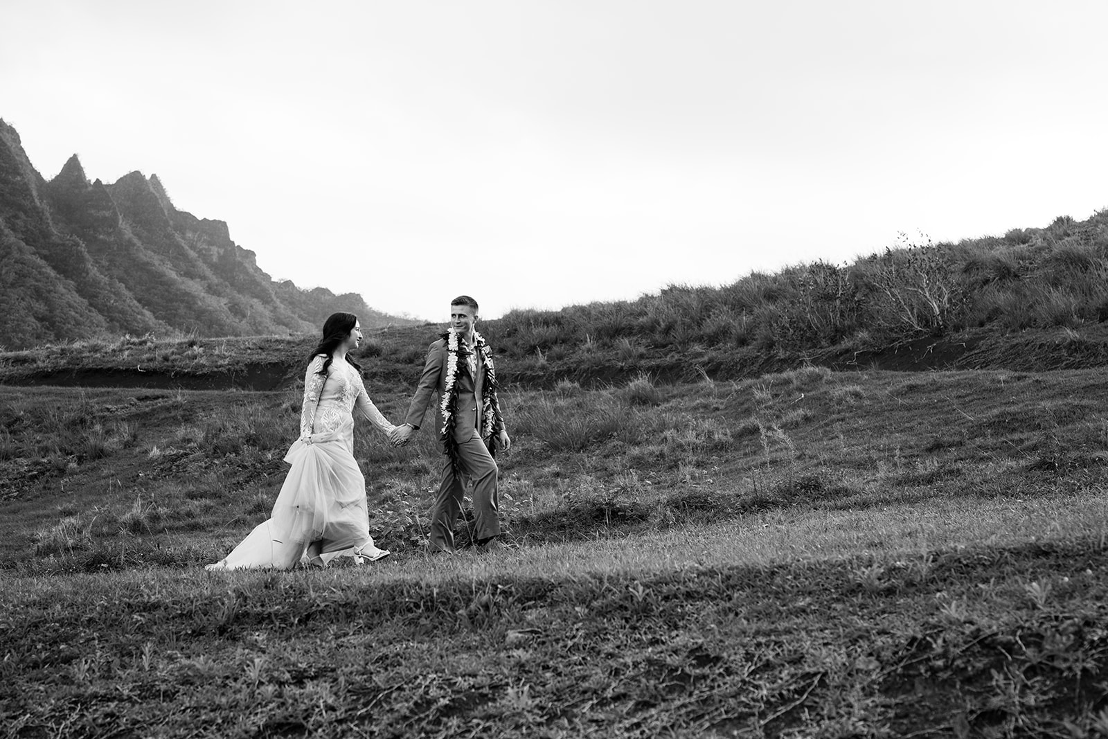 A black and white photo of a bride and groom walking in a field at their destination wedding.