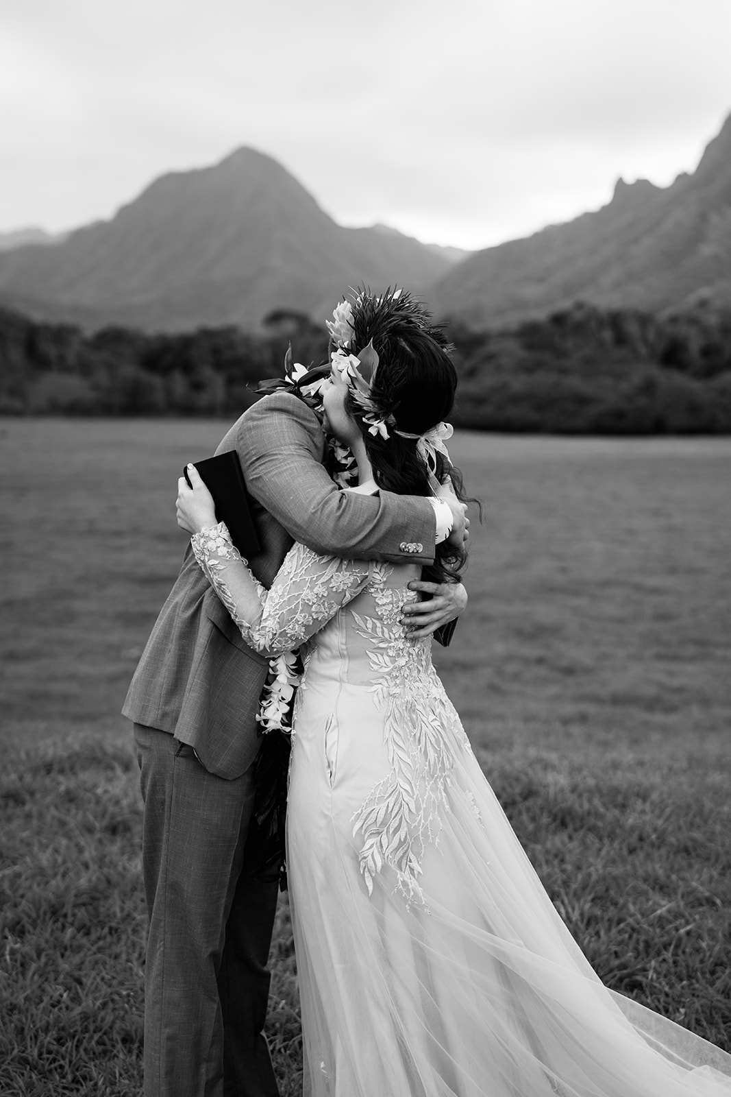 A bride and groom hugging in a field at Kualoa Ranch, perfectly captured by a Hawaii Wedding Photographer.