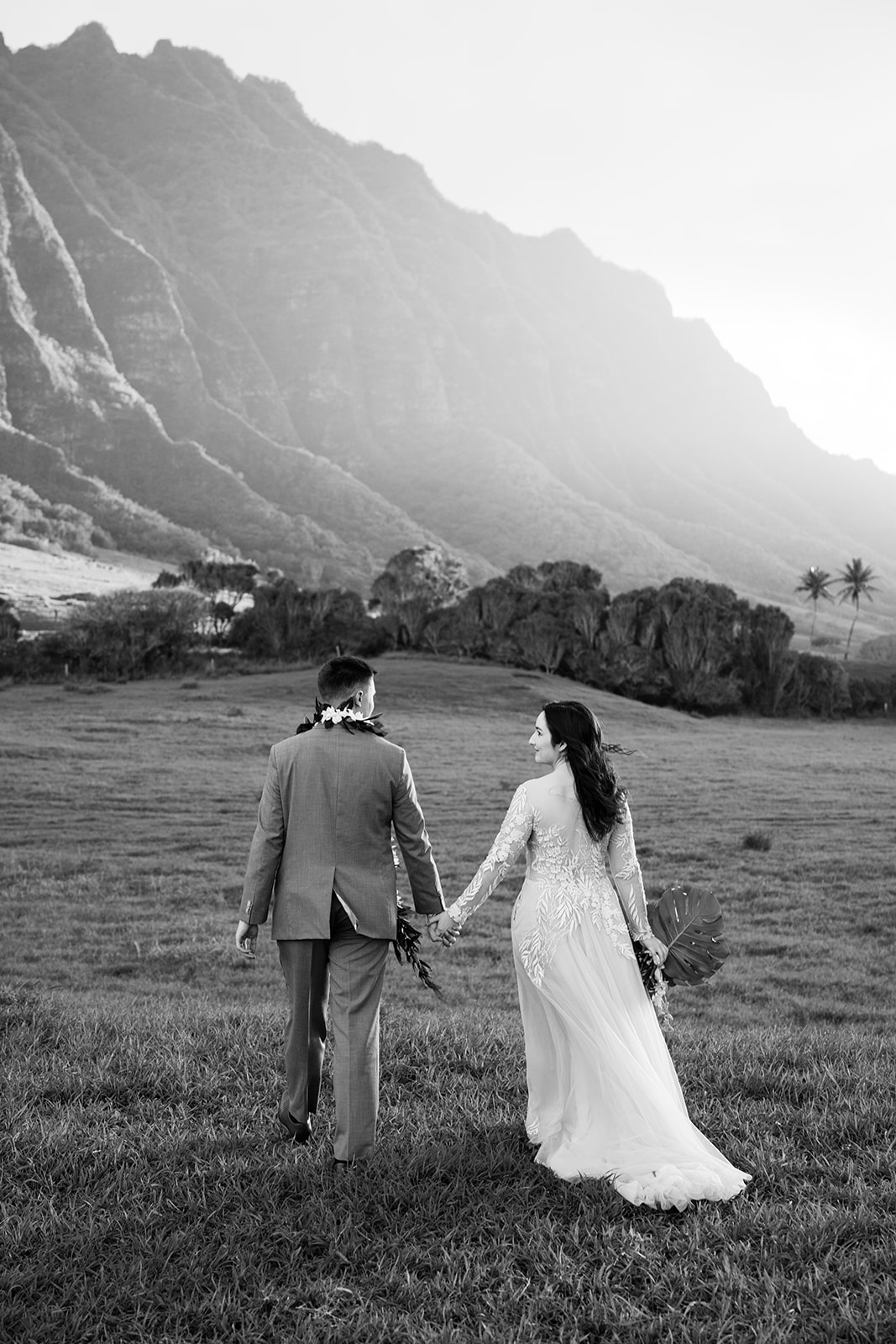 A man and woman holding hands in a field with mountains in the background.