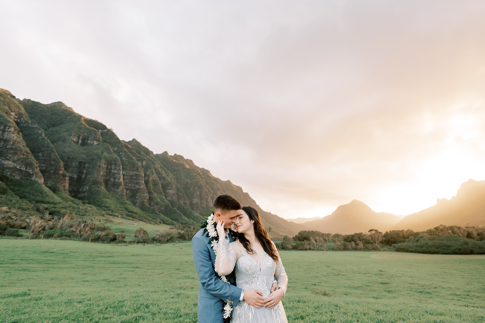 A bride and groom embrace in a grassy field during their hawaiian elopement.