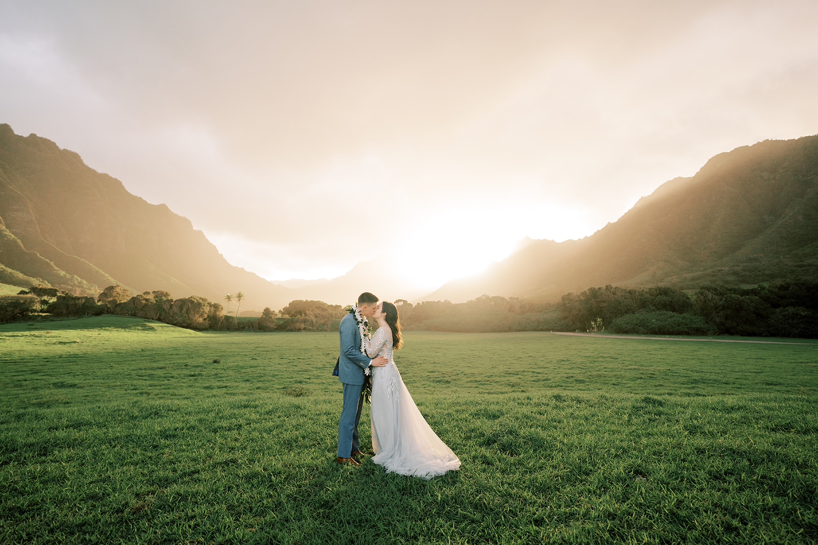 A bride and groom standing in a grassy field at sunset during their Kualoa Ranch wedding.