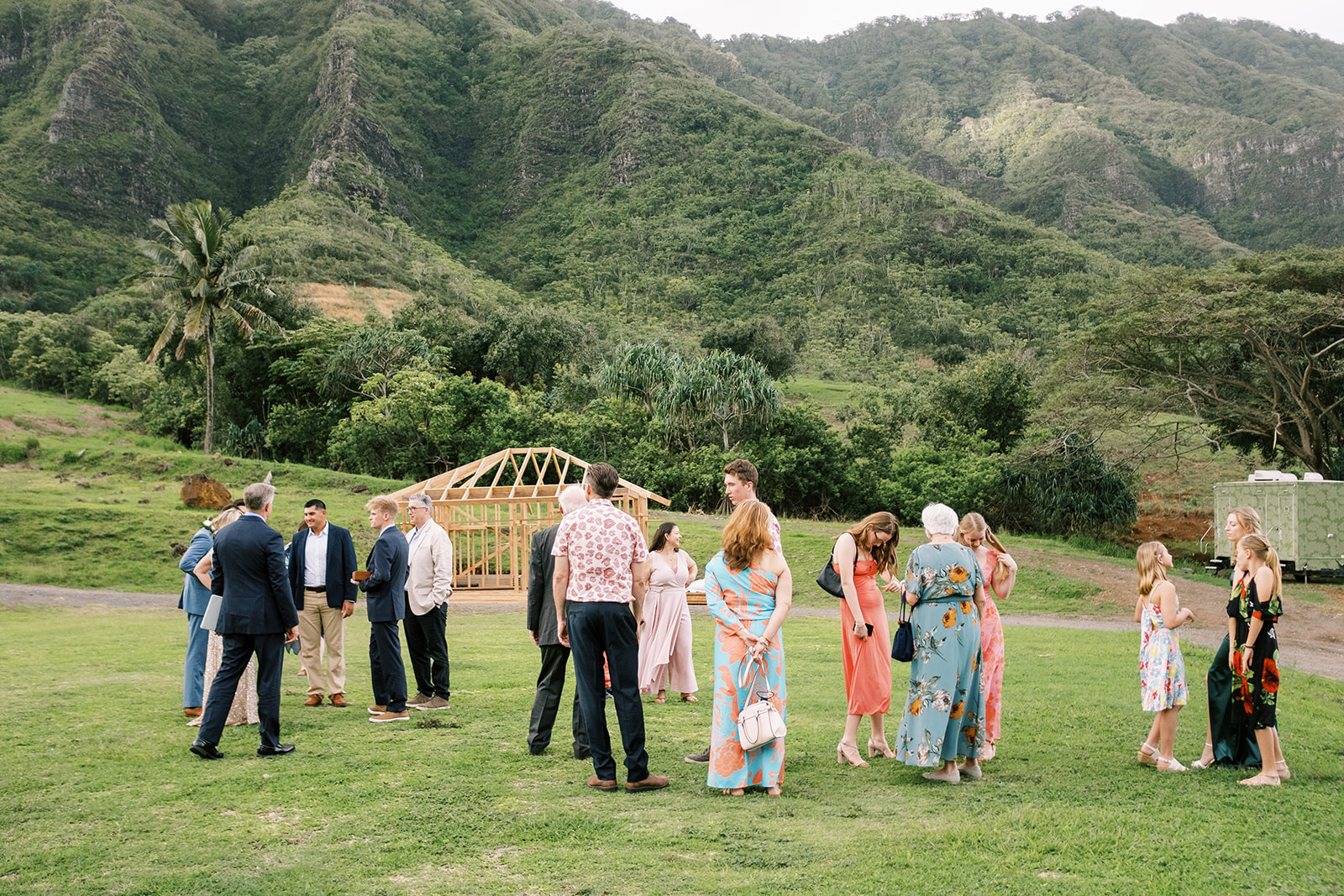 A group of people standing in a grassy field during a wedding with mountains in the background.