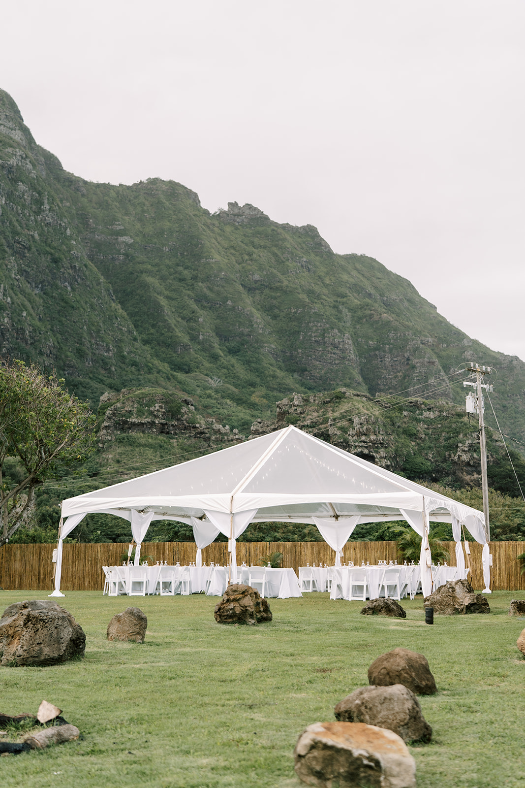 A white tent at a Kualoa Ranch destination wedding in a grassy field with mountains in the background.