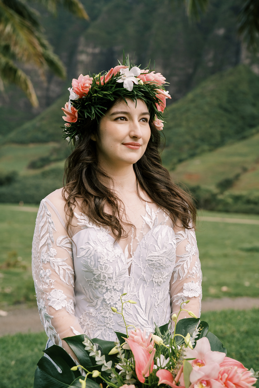 A bride in a white dress with a flower crown in front of a palm tree at a Kualoa Ranch wedding.