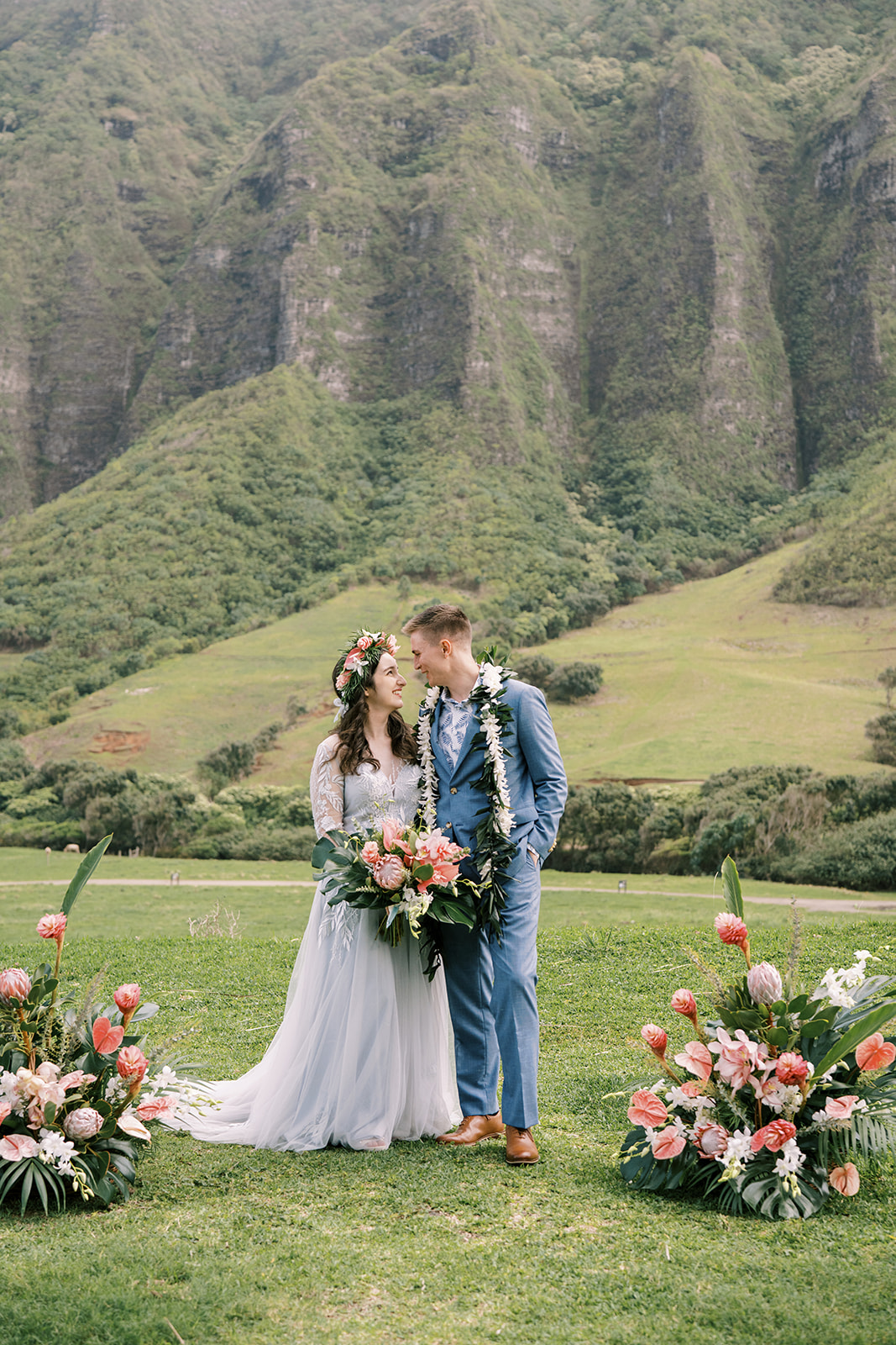 A man and woman in wedding attire standing in front of a mountain at a Kualoa Ranch Wedding.