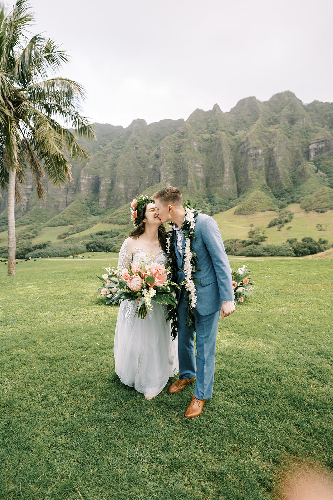A bride and groom kissing in the grass with palm trees in the background at a Kualoa Ranch Wedding.