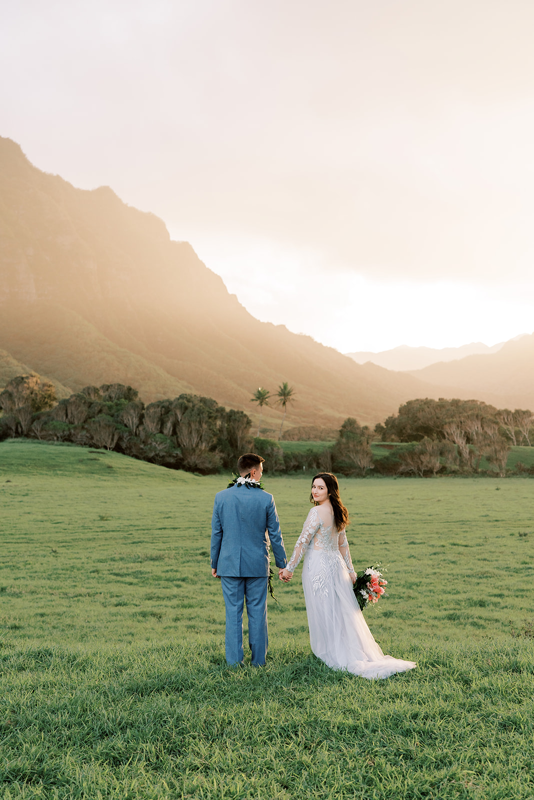 A man and woman holding hands in a field at Kualoa Ranch Wedding, with mountains in the background.