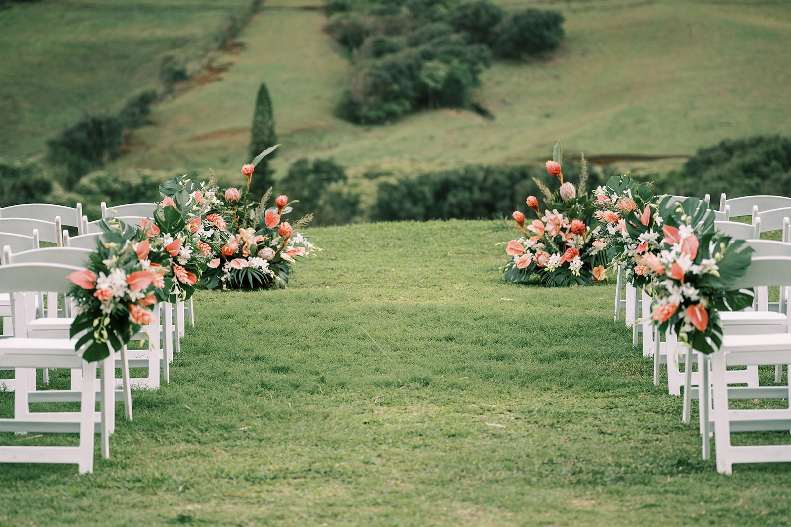 A white wedding ceremony set up in a grassy field at Kualoa Ranch, with mountains in the background.