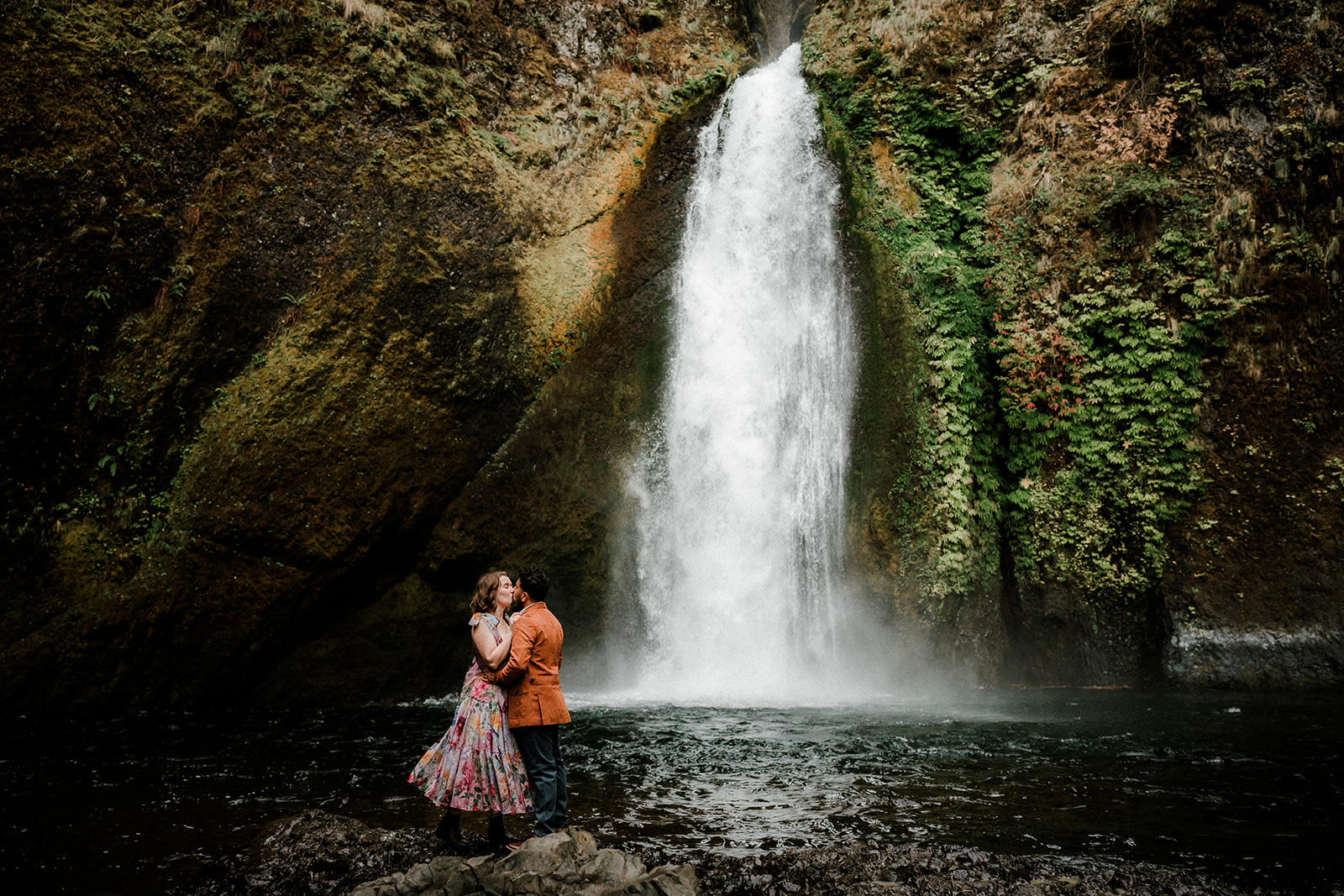 engaged couple embracing at the base of Wahclella Falls in the Pacific Northwest