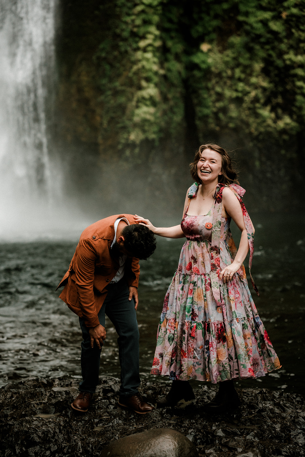 Romantic couple in colorful dress exploring the lush pacific northwest wahclella falls waterfall for engagement photos