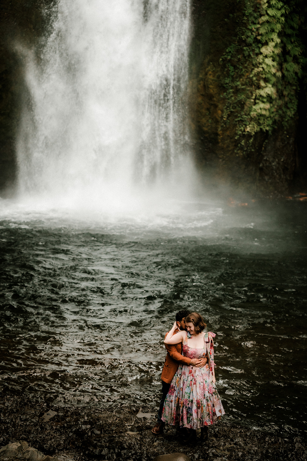 Romantic couple in colorful dress exploring the lush pacific northwest wahclella falls waterfall for engagement photos