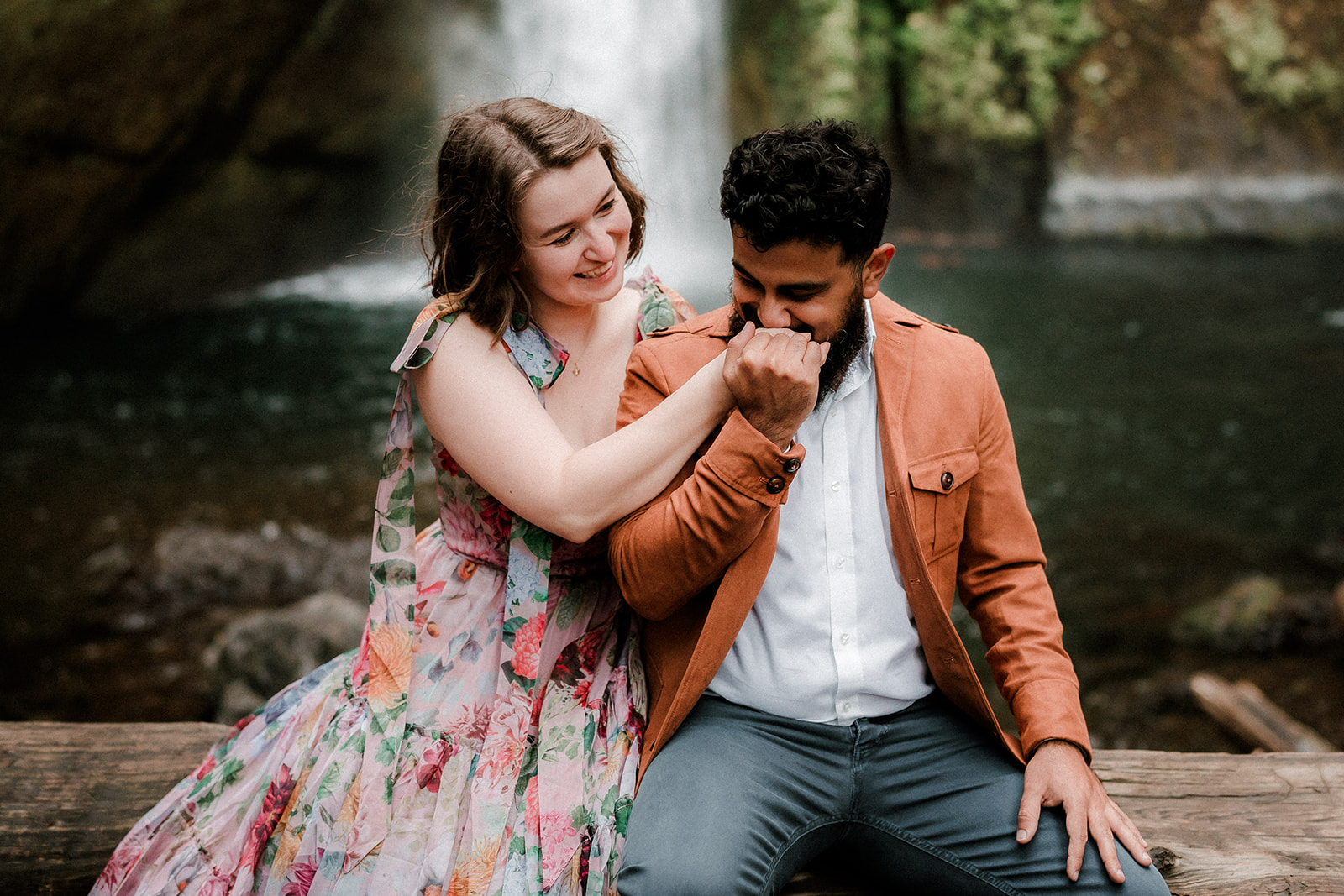 couple sitting on log pile in front of Wahclella Falls for their engagement photo session in Portland, OR