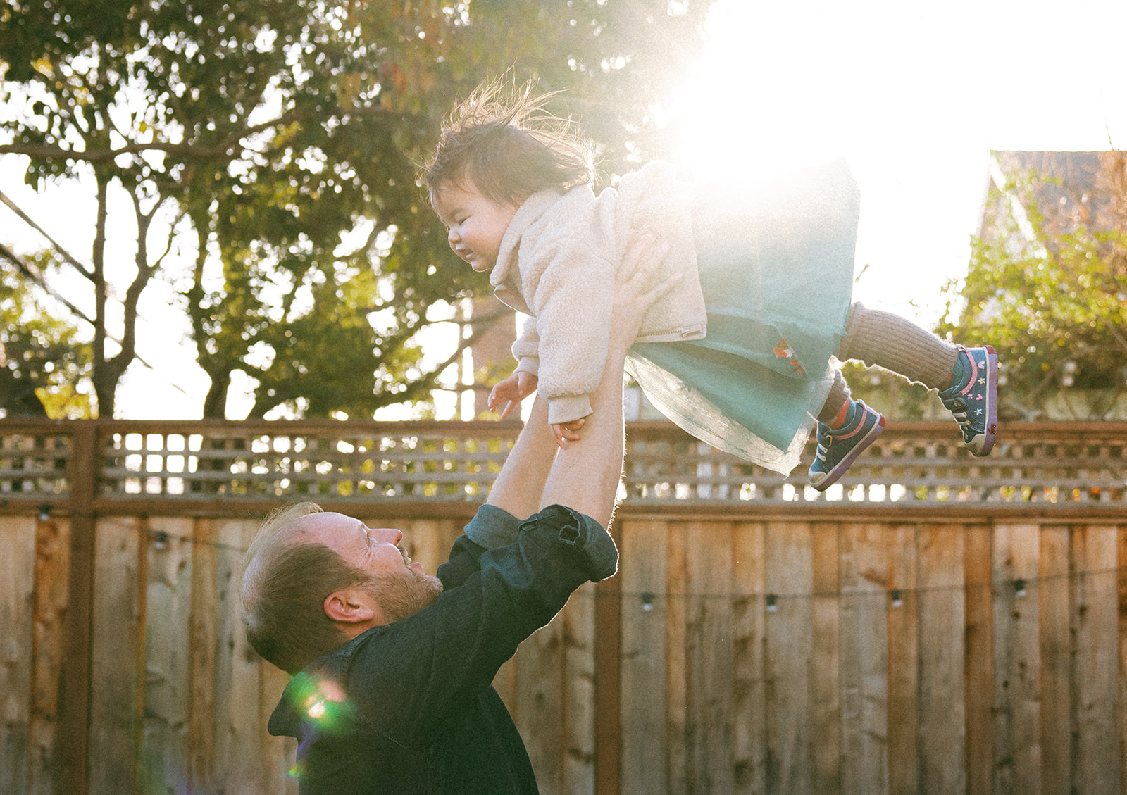 dad throwing baby daughter in the air in their backyard at golden hour