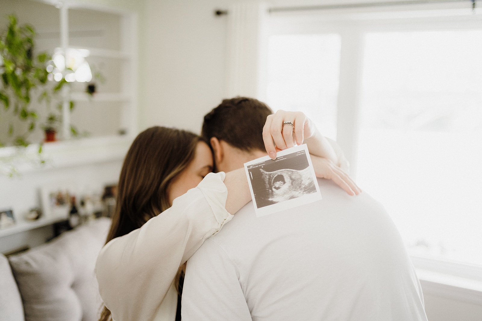 A woman hugging a man around his neck while holding a picture.
